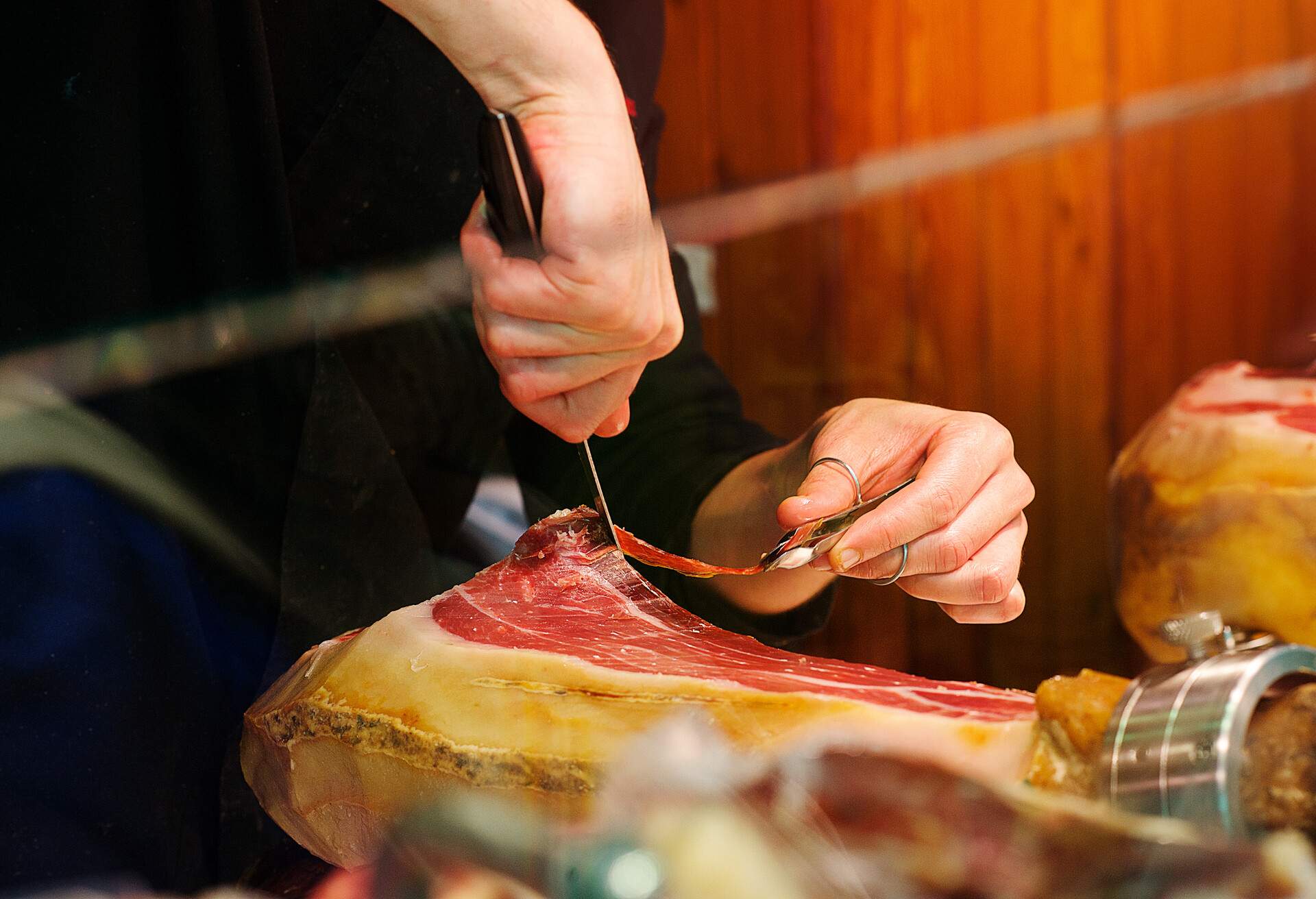 A hand cutting a thin piece of ham.