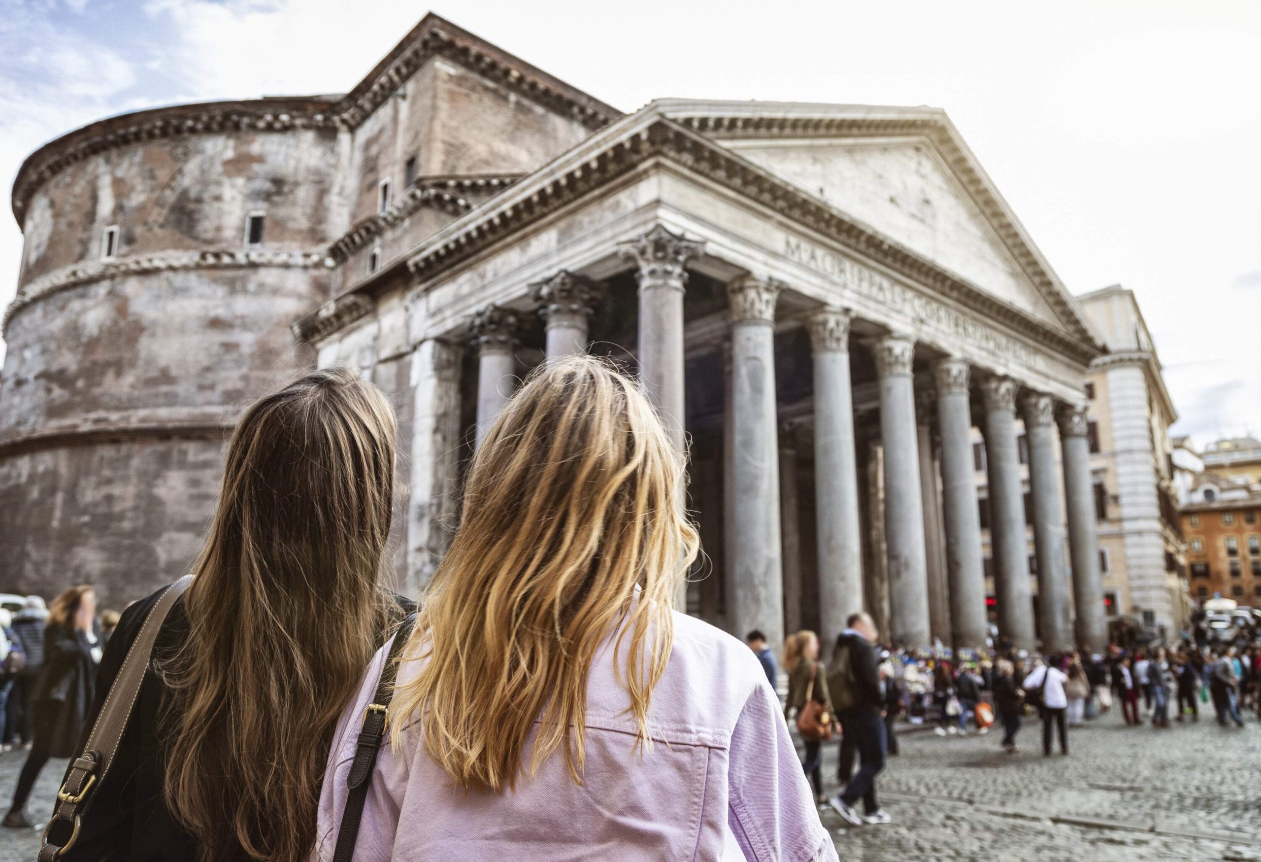 Two women gazing towards the Pantheon and the people passing by across the piazza.