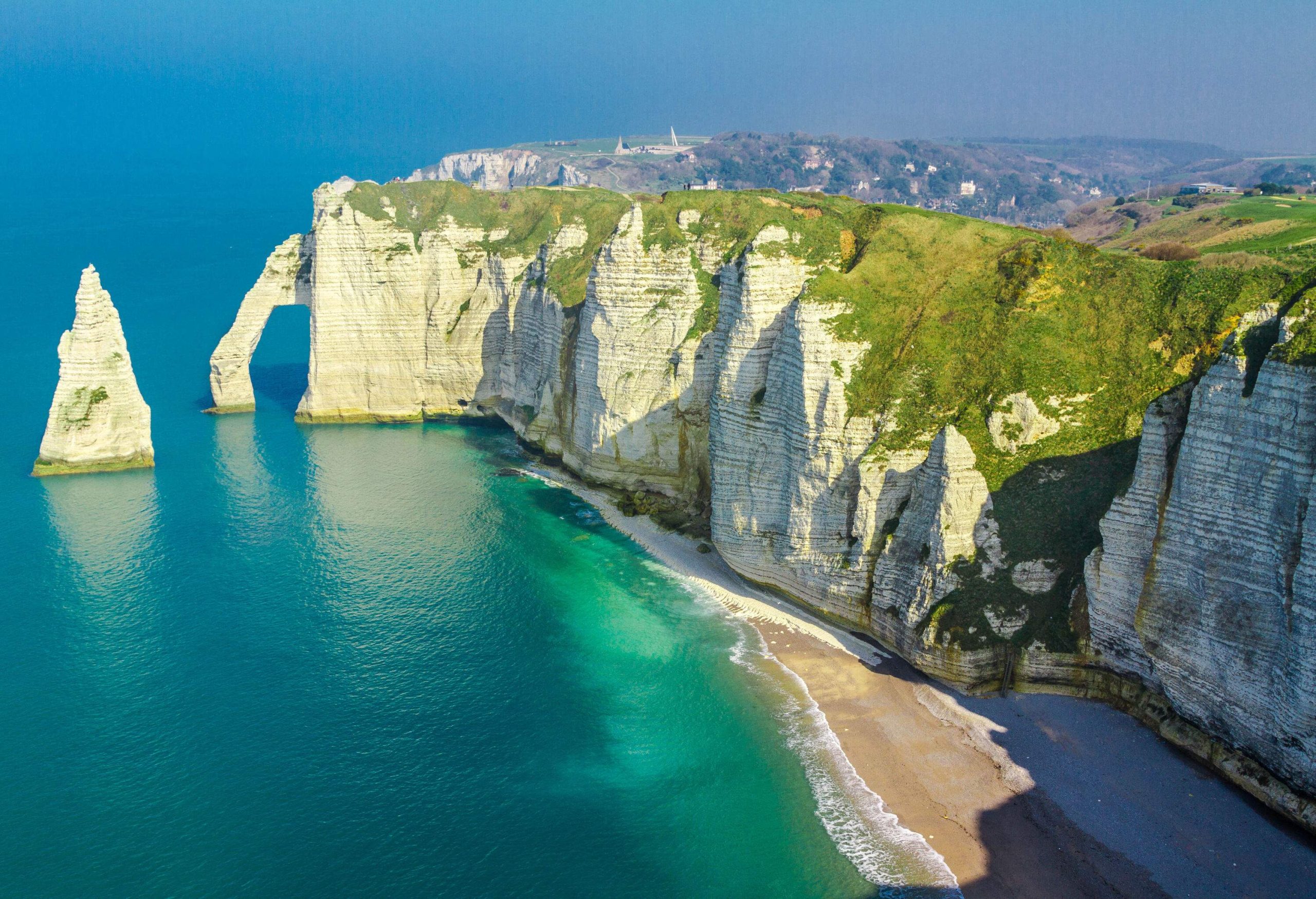 Steep white cliffs along a coastline with a pointed rock formation in the ocean.