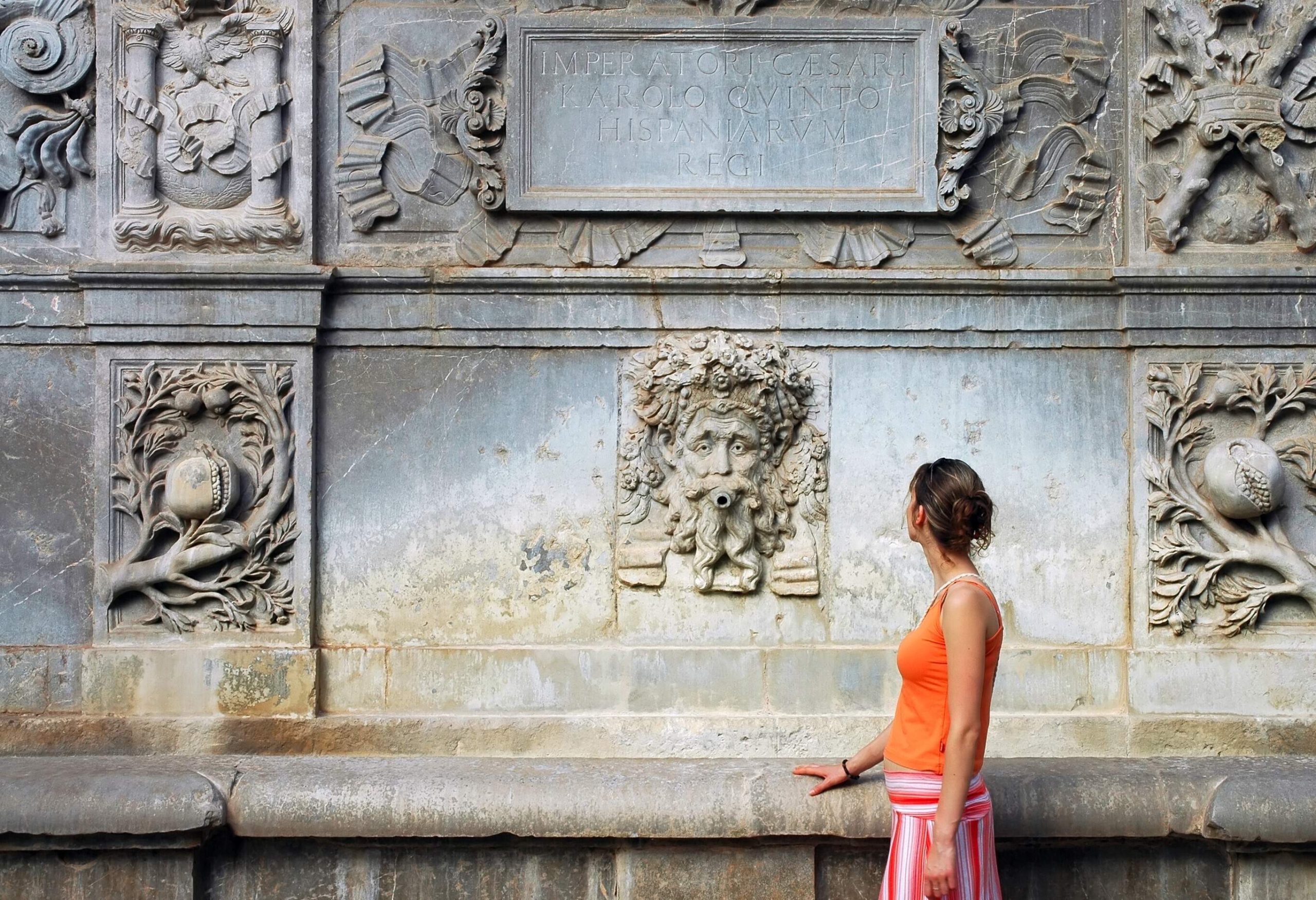 A lady tourist stares blankly at the ornate carvings on the stone wall.
