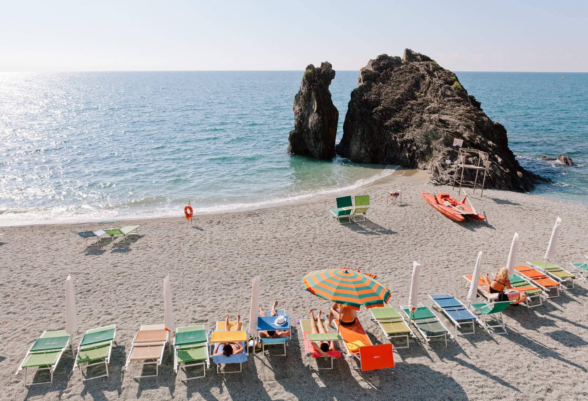 vacation beach with colorful rainbow chaise lounge chairs and umbrellas. resort beach. Monterosso, Cinque Terra, Italy. old fishing village and tourist destination
