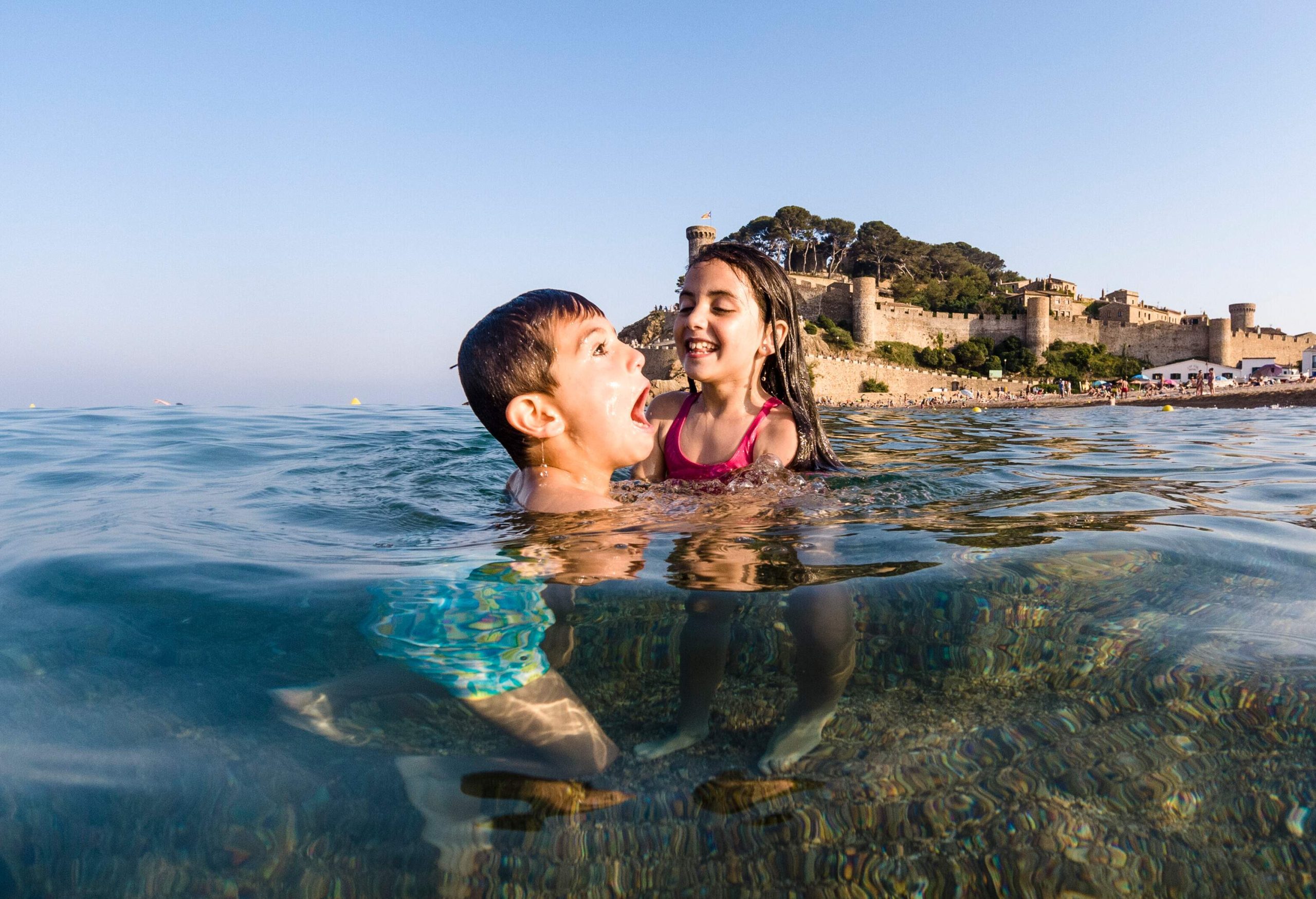 A couple of children playing in the sea with a fortress in the background.