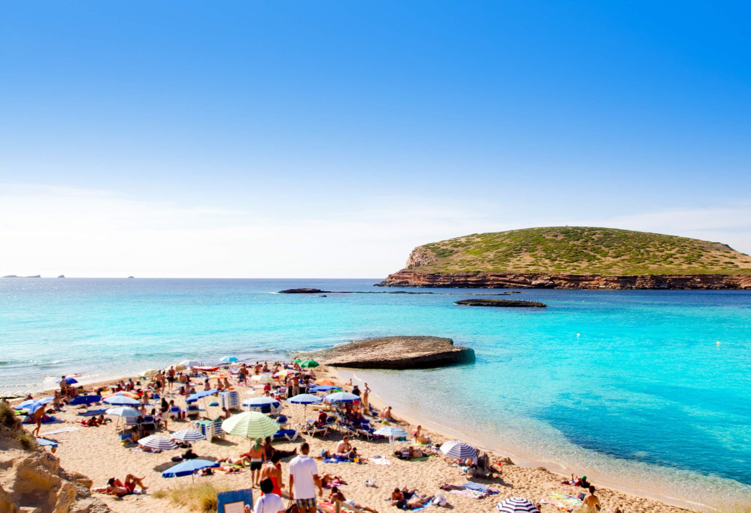 People hanging out on a sunny day at the beach with clear blue waters.