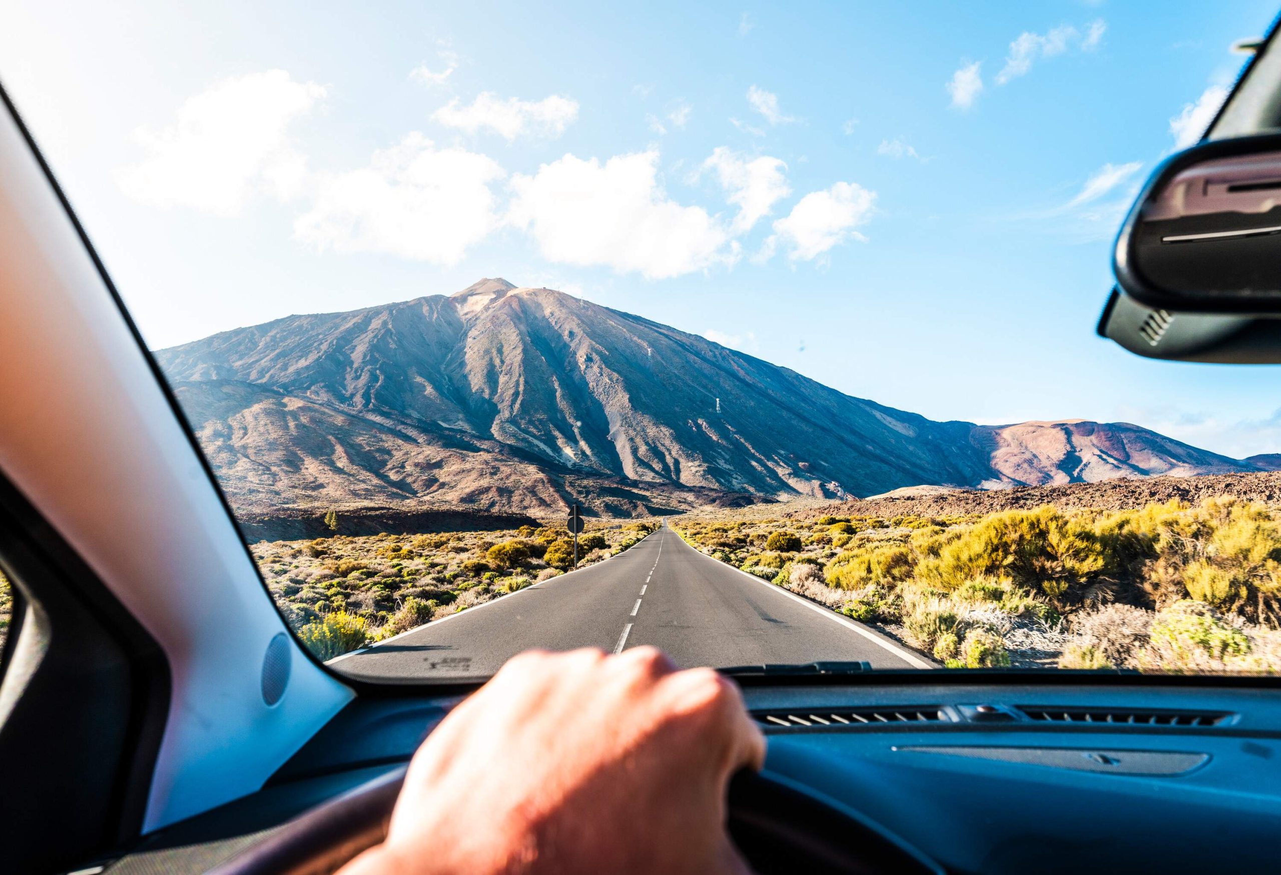 A man driving down a road with a big mountain in the distance.