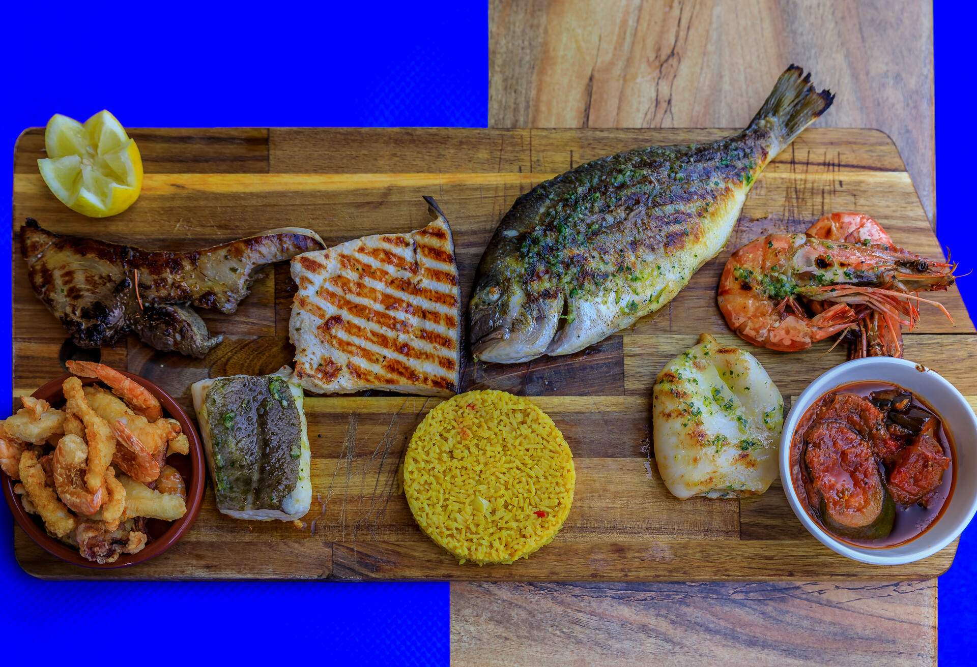 Selection of fish and seafood with shrimp and calamari served with rice and sauteed vegetables on a board at a Corsican restaurant in Nice, France