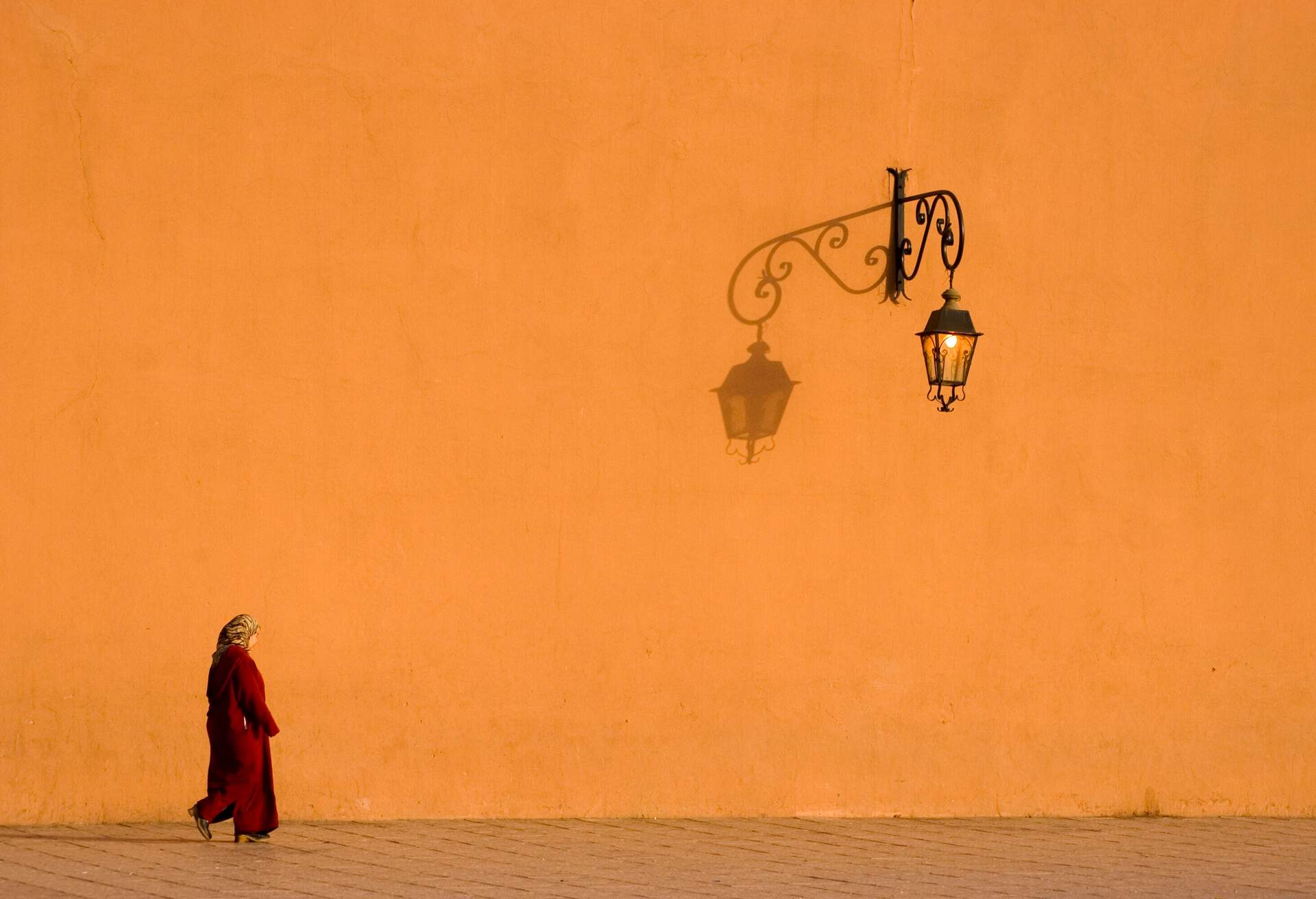 Moroccan woman walking next to a sunlit wall.