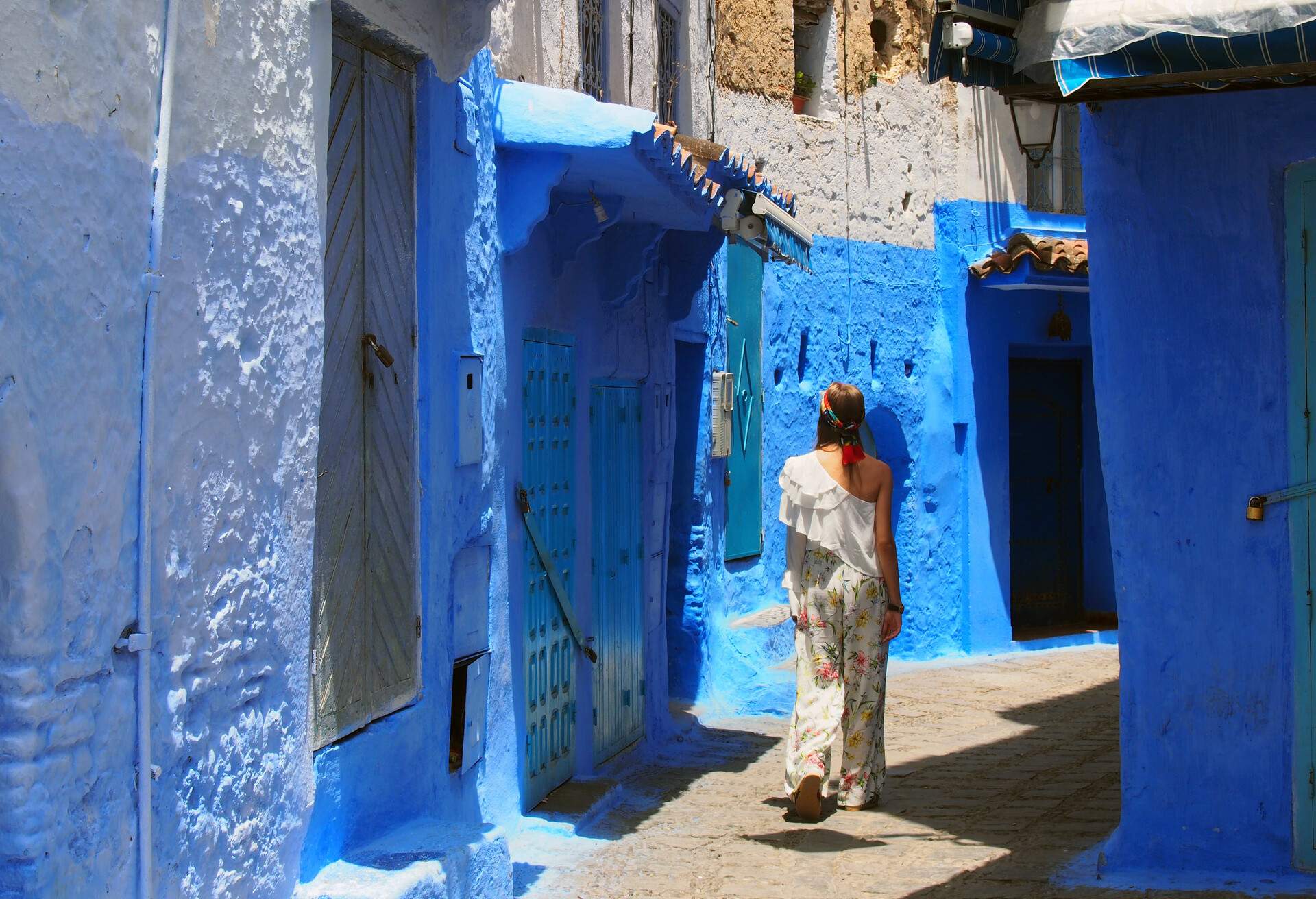 Tourist walking on the blue streets of Chefchaouen, Morocco. Blonde woman in white clothes admiring the medina of the Blue City in Morocco, Africa. Narrow alley with blue houses in Chefchaouen; Shutterstock ID 693855895; Purpose: ; Brand (KAYAK, Momondo, Any):