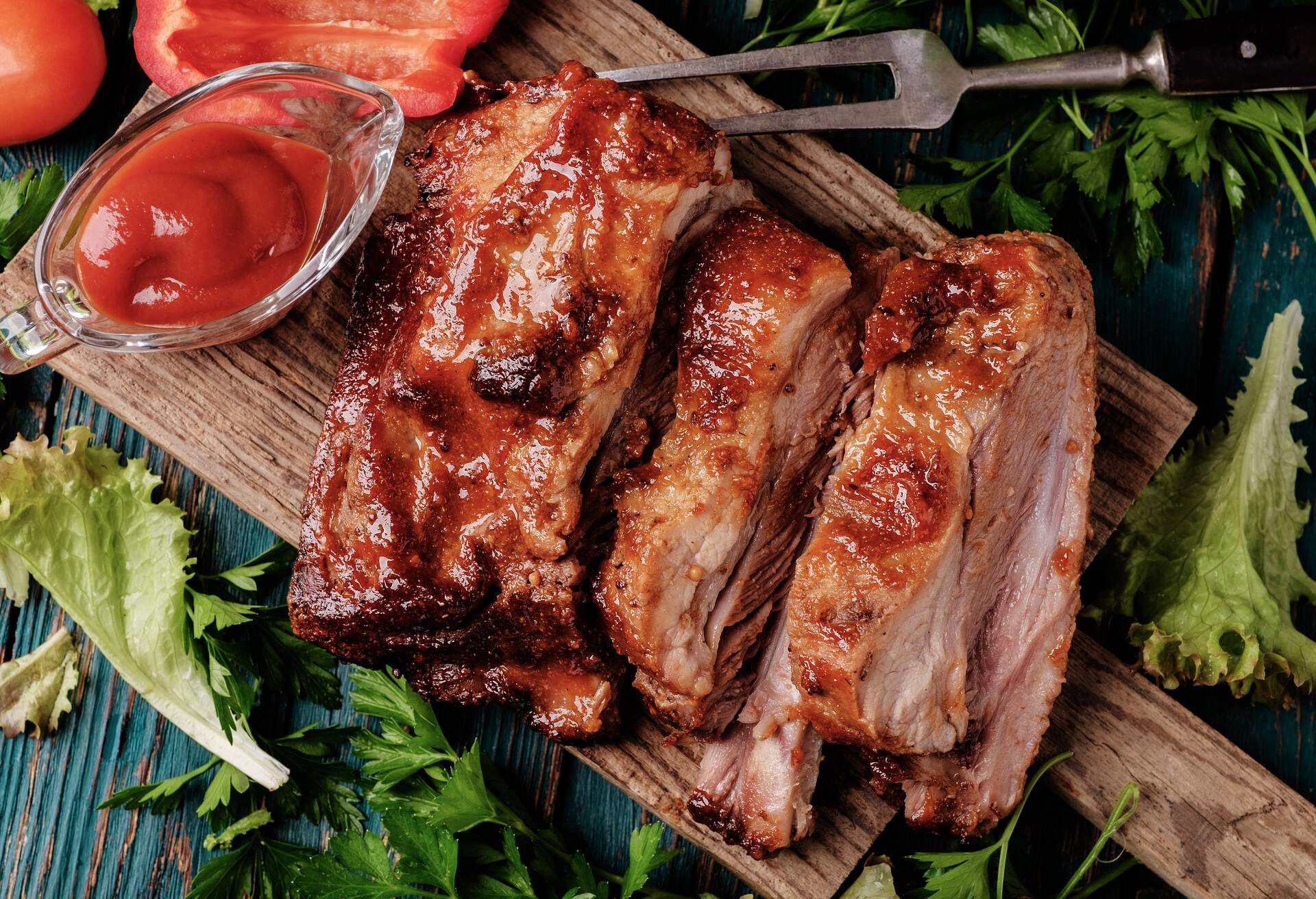 Delicious barbecued ribs seasoned with a spicy basting sauce and served with chopped fresh vegetables on an old rustic wooden chopping board in a country kitchen. Top view.