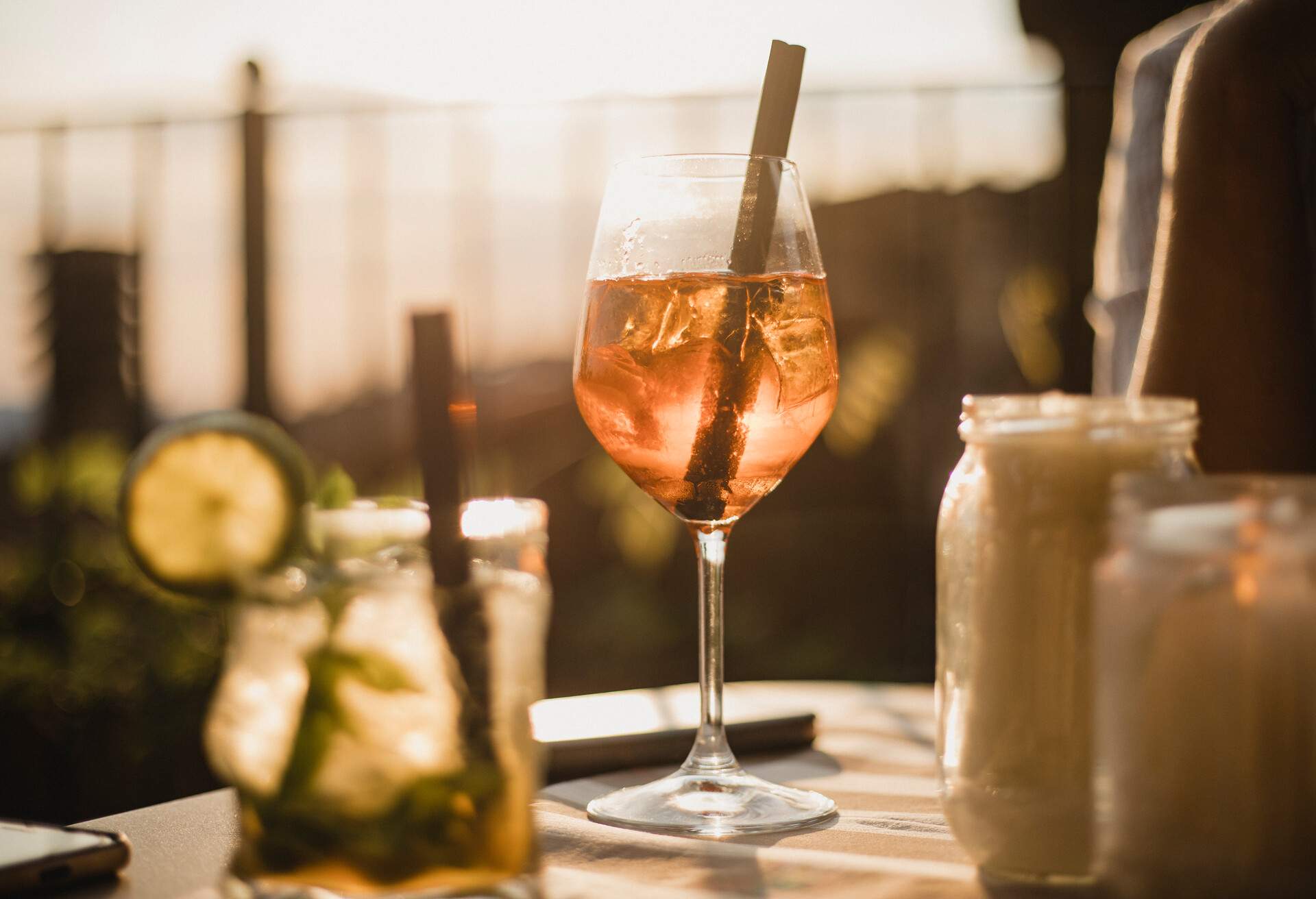 Two alcoholic drinks sitting on a table with a sunset in the background shining through. There are no people in the image with the drinks.