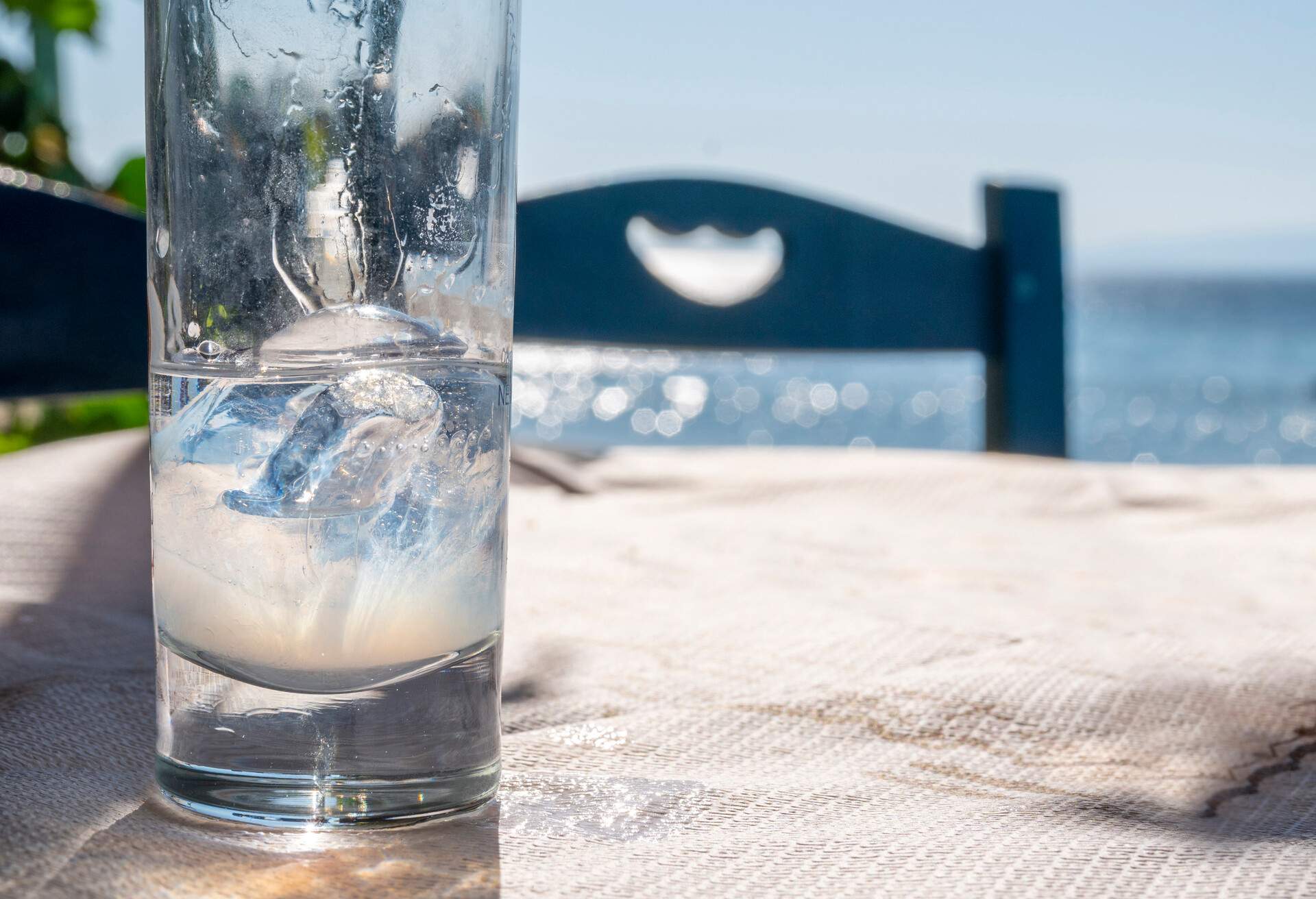 A Greek traditional spirit, glass of ouzo under sunlight, at the beach restaurant table.