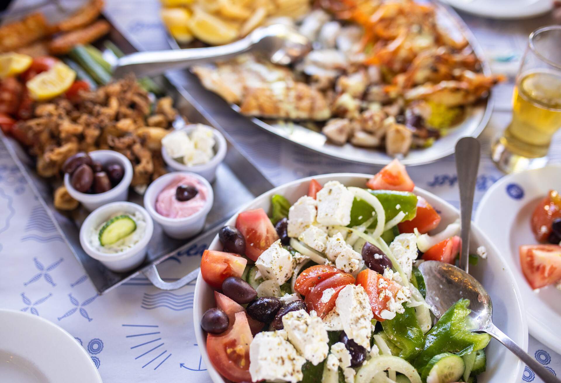 Greek salad, fresh vegetables, feta cheese and black olives in bowl and seafood on table