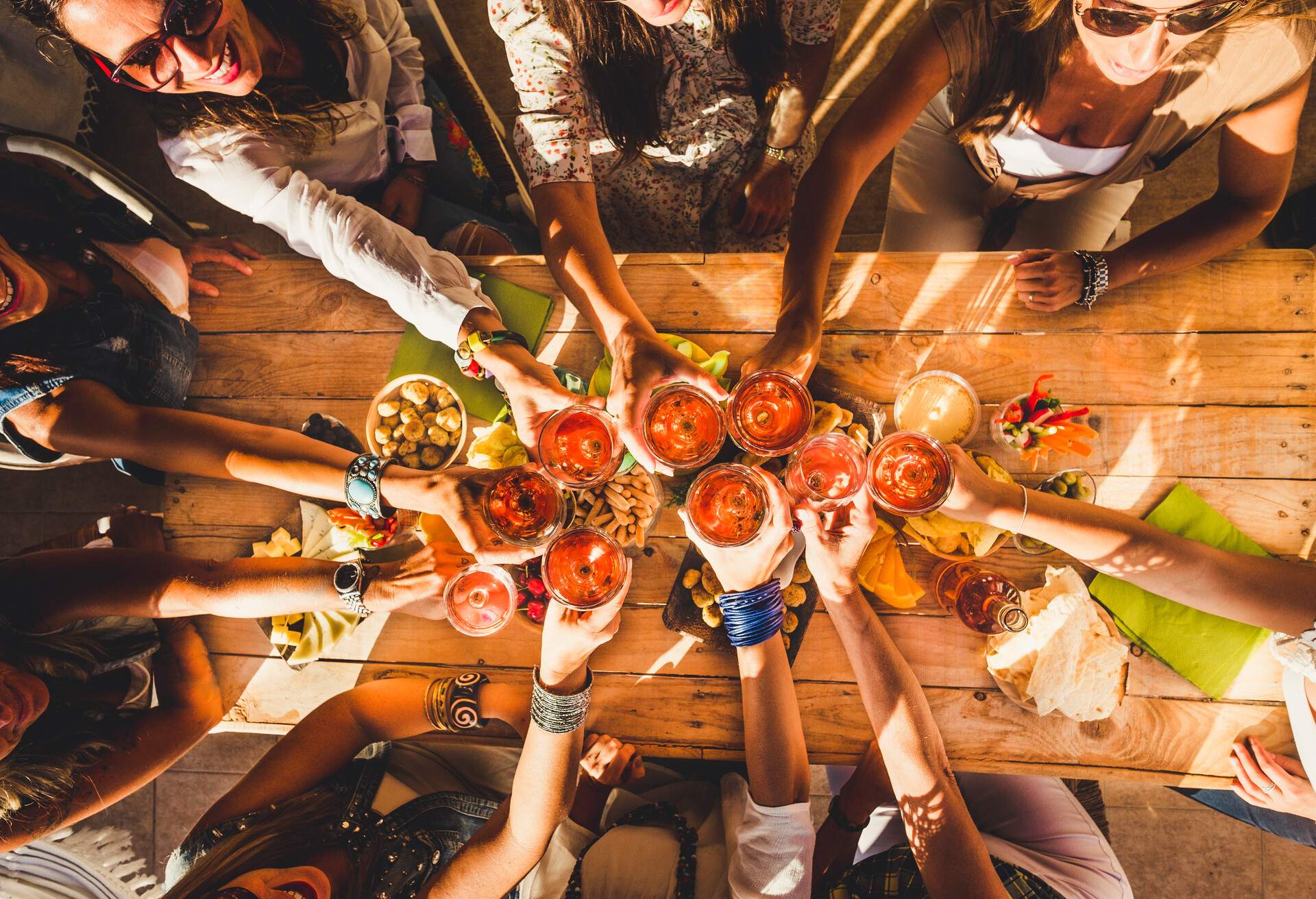 Above view group of friends people enjoy food and drinks toasting and clinking with red wine glasses all together having. fun - celebration and friendship concept - coloured background