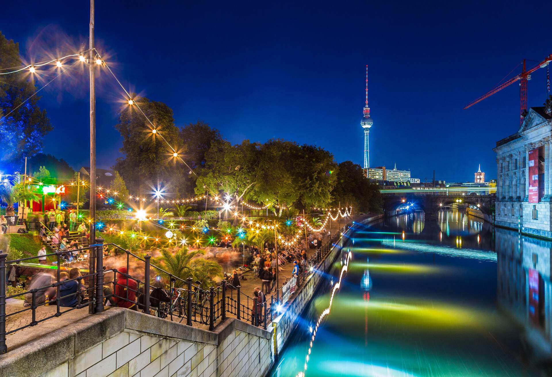 People enjoying a night out at a riverside bar decorated with colourful hanging lights.