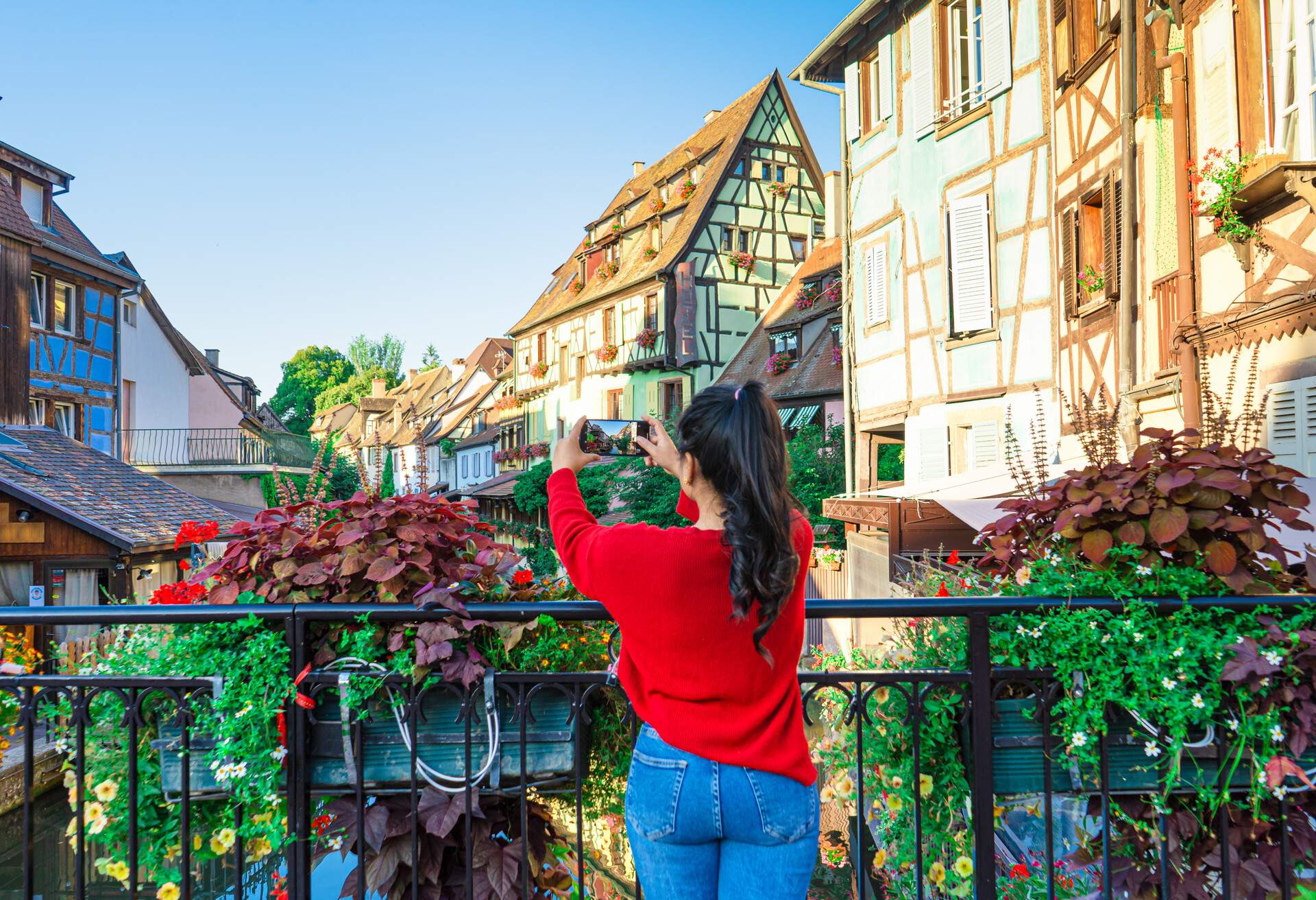 A female on a bridge takes a picture of the traditional half-timbered houses by the canal.