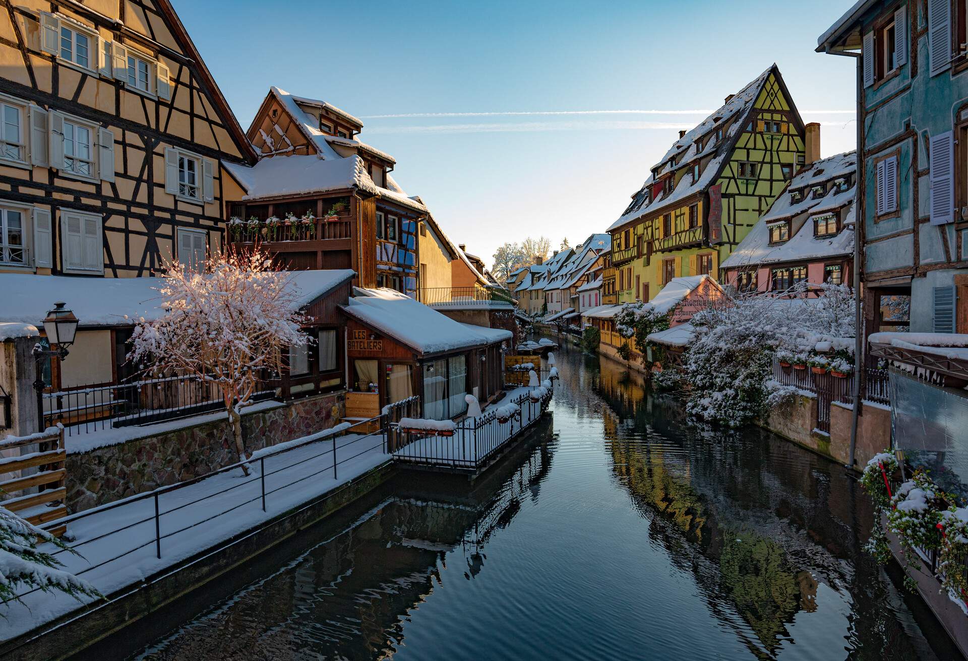 Snow-covered colourful french houses lined on both sides of a river.