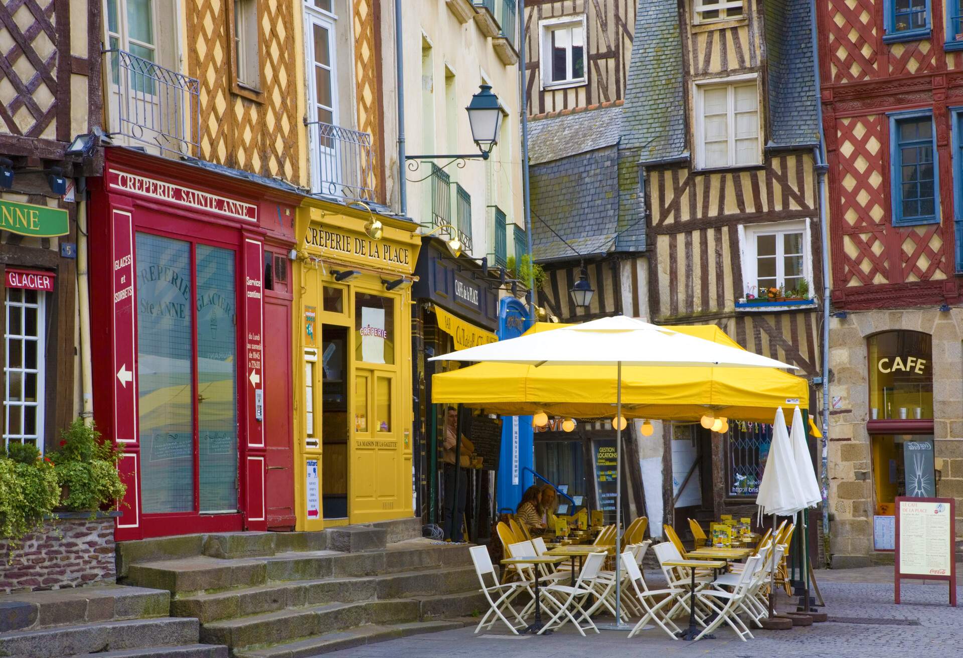 Colourful shops and cafes with outdoor seating under yellow umbrellas on the sidewalk.