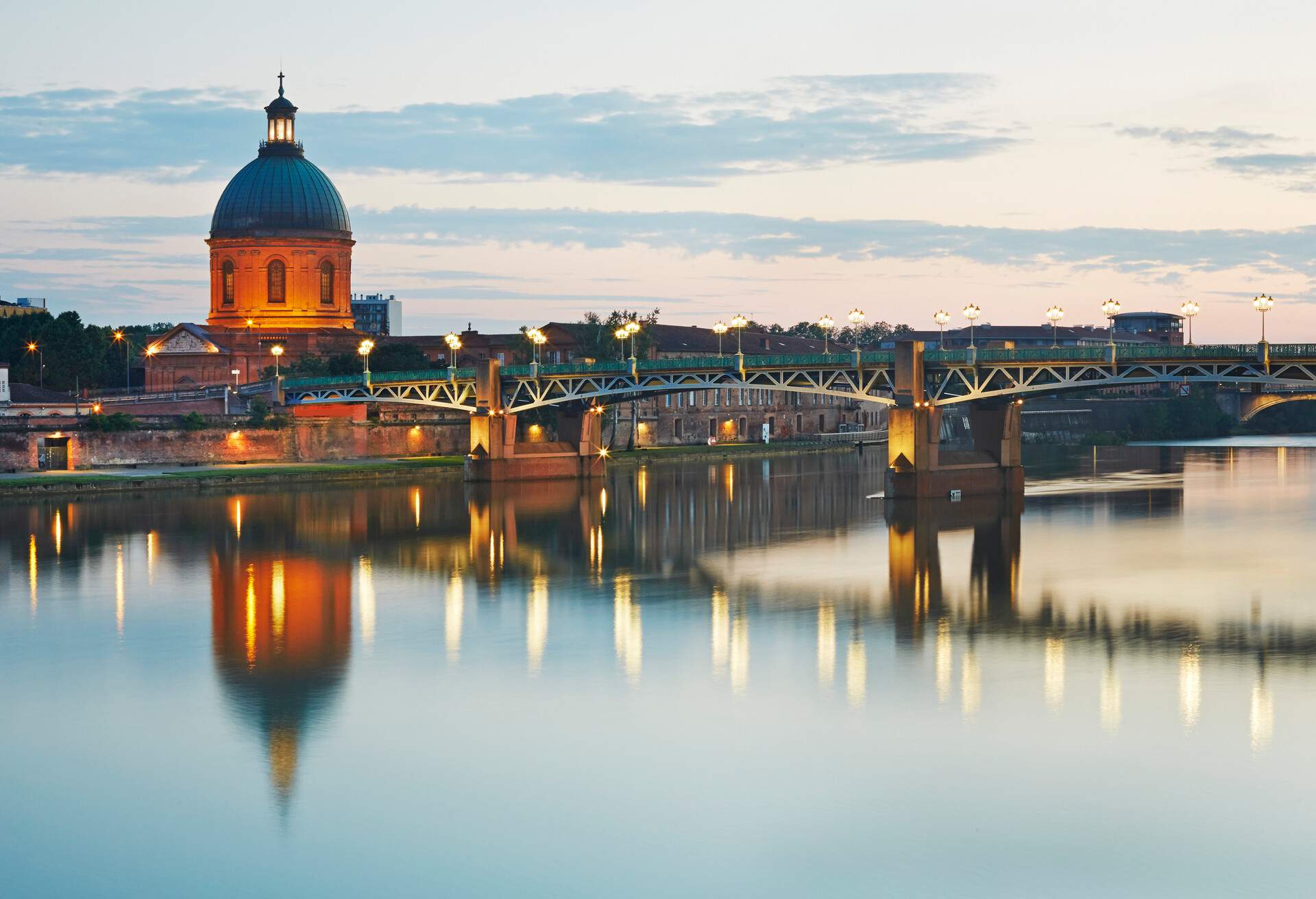 The dome of the 'Hopital de la Grave' with 'Pont Saint -Pierre' girder bridge illuminated at dusk over the Garonne River