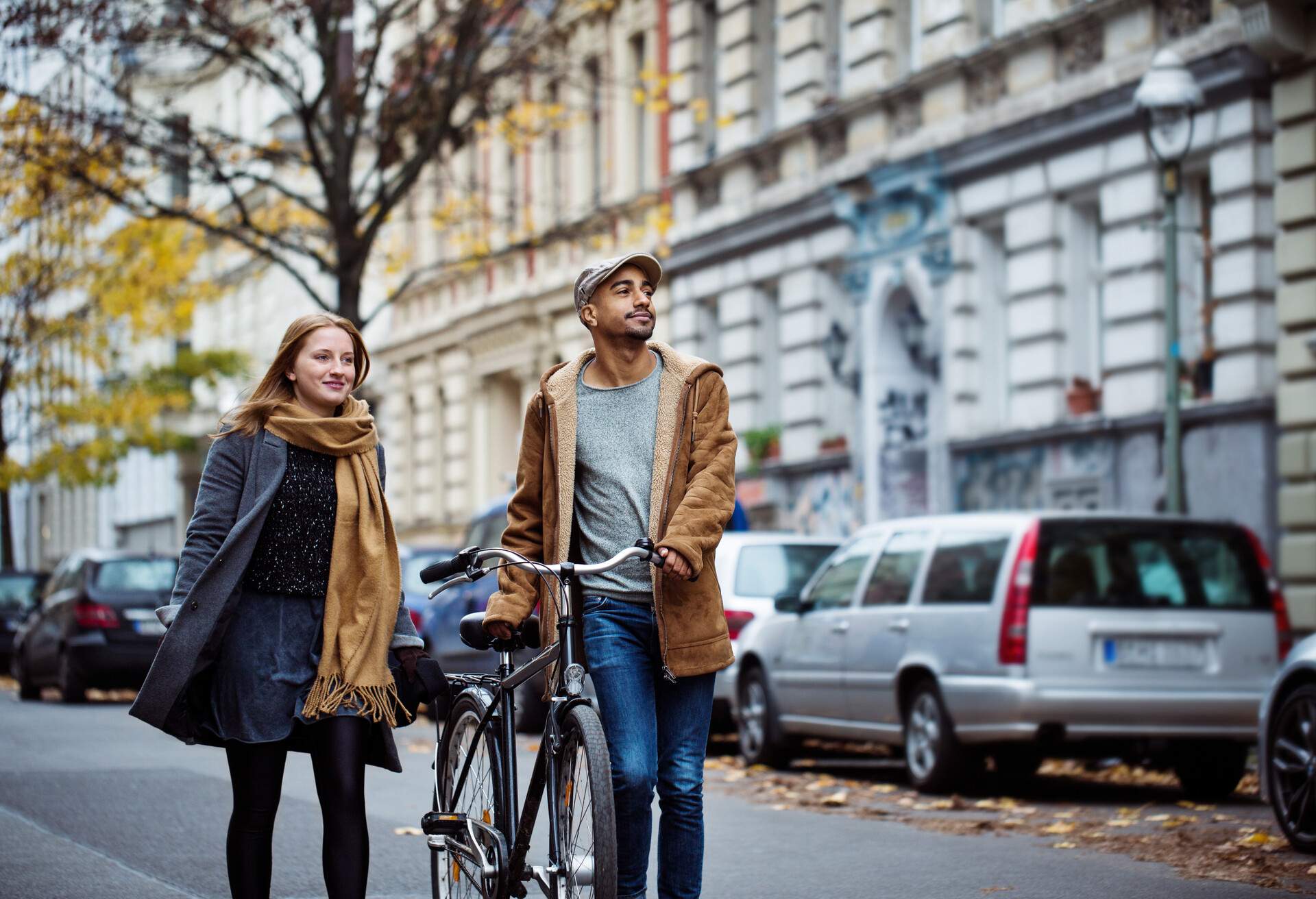 A man and a woman in winter clothes walk down a street with a bicycle.