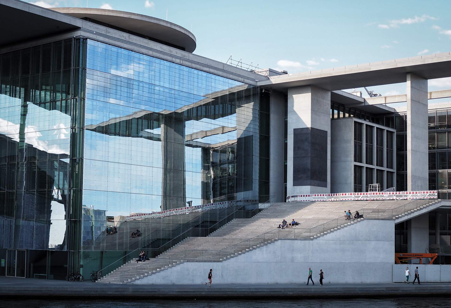 A group of people lounge on the massive outdoor staircase of a modern building with glass façade.