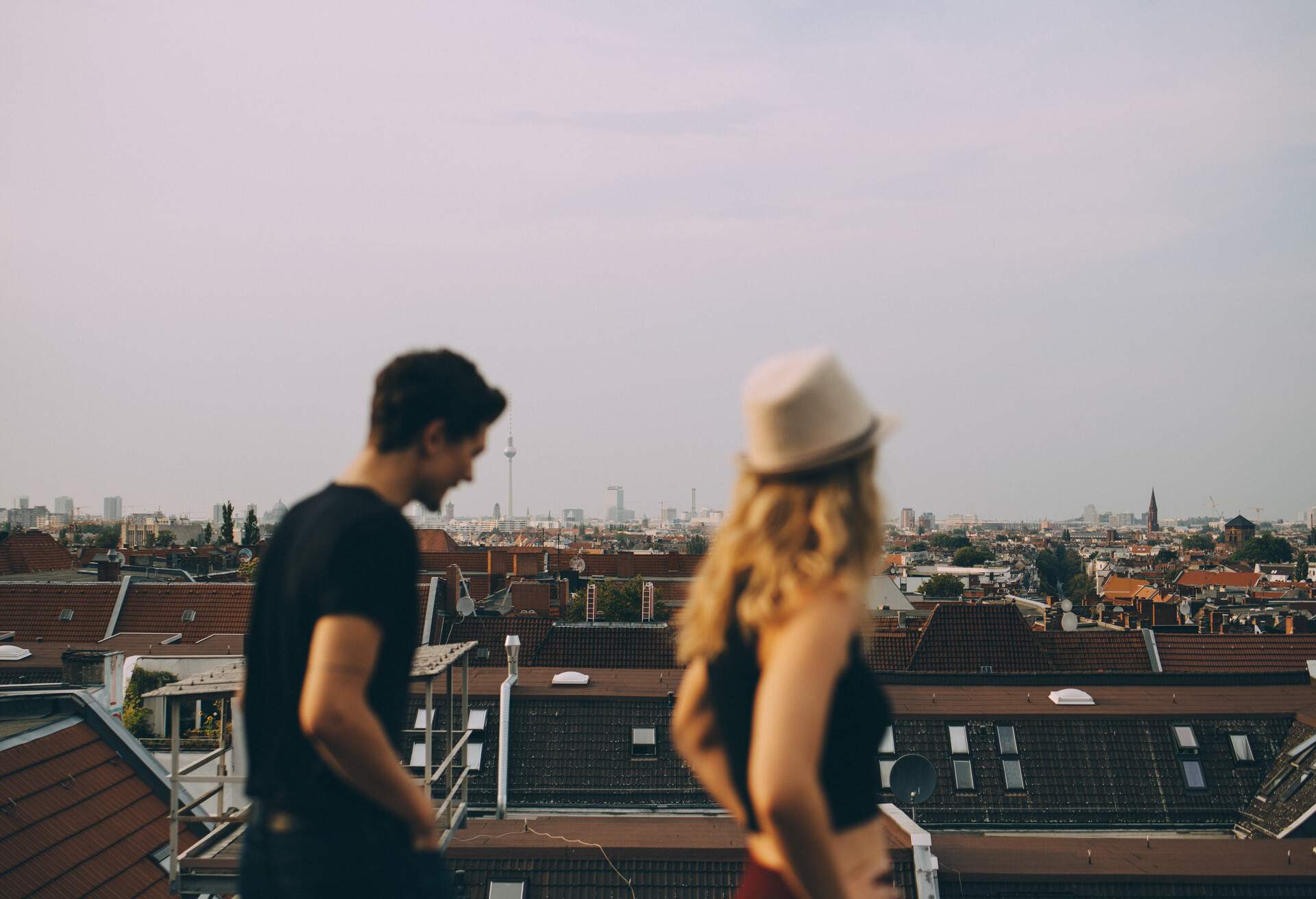 A man and a blonde woman stand on a rooftop as they gaze at the vast cityscape.