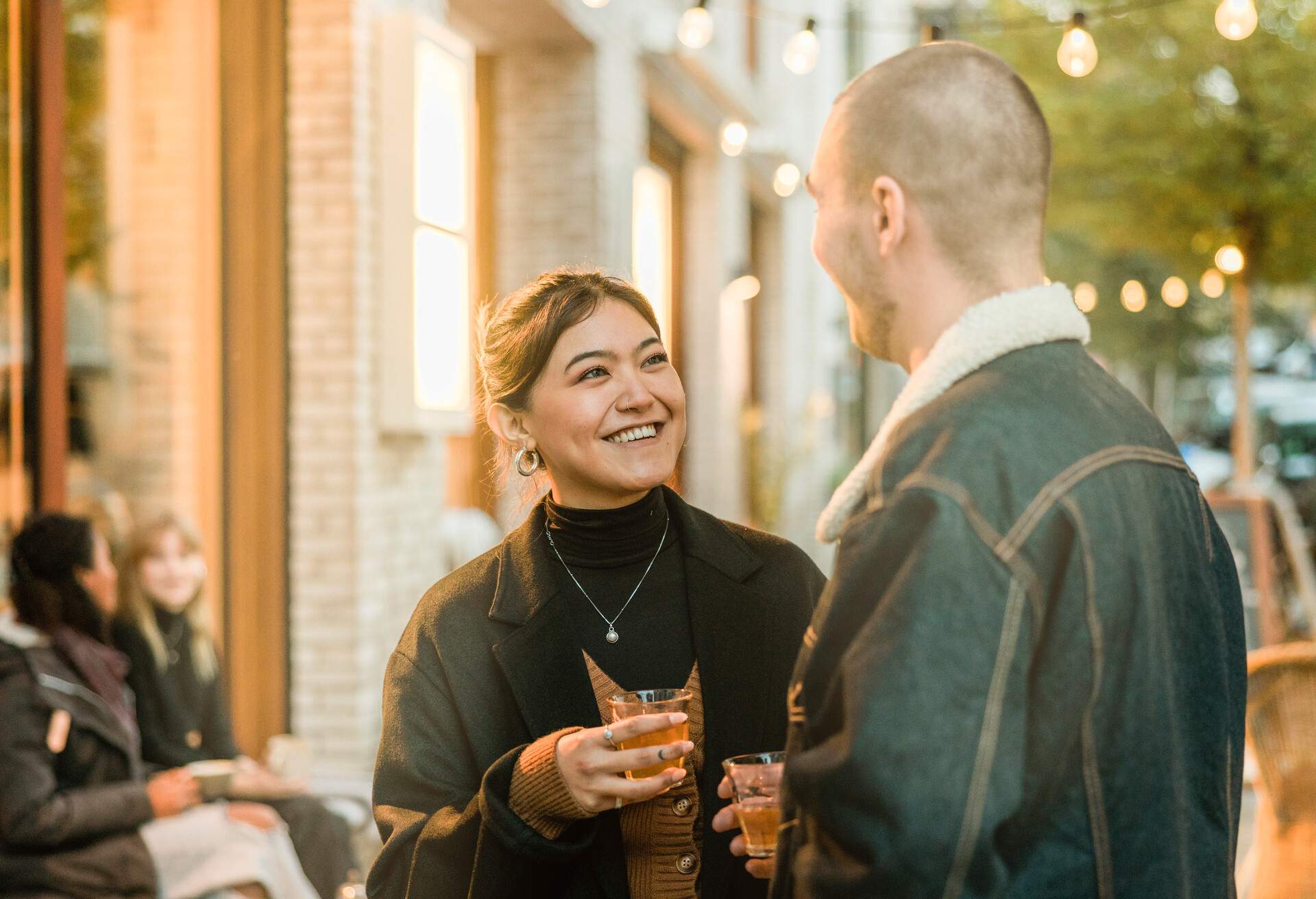 A couple chatting and smiling outside while enjoying a warm cup of tea in the cold.