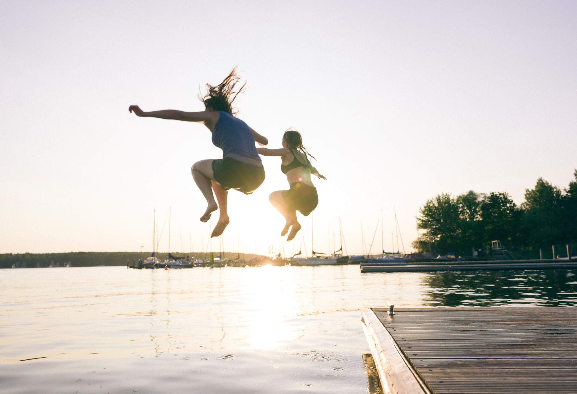 Two people leap into the air above a lake in a harbour.