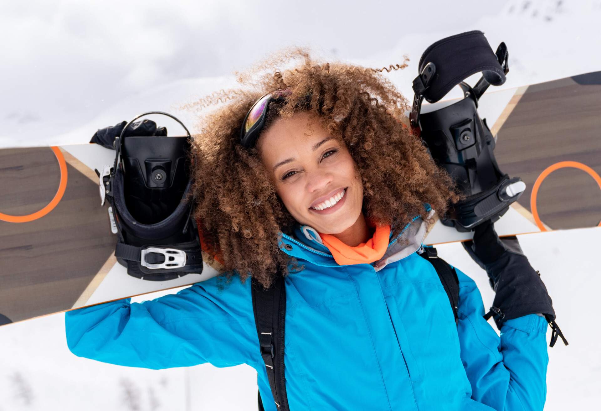 Portrait of a happy beautiful black woman snowboarding looking at the camera smiling - winter sports lifestyle