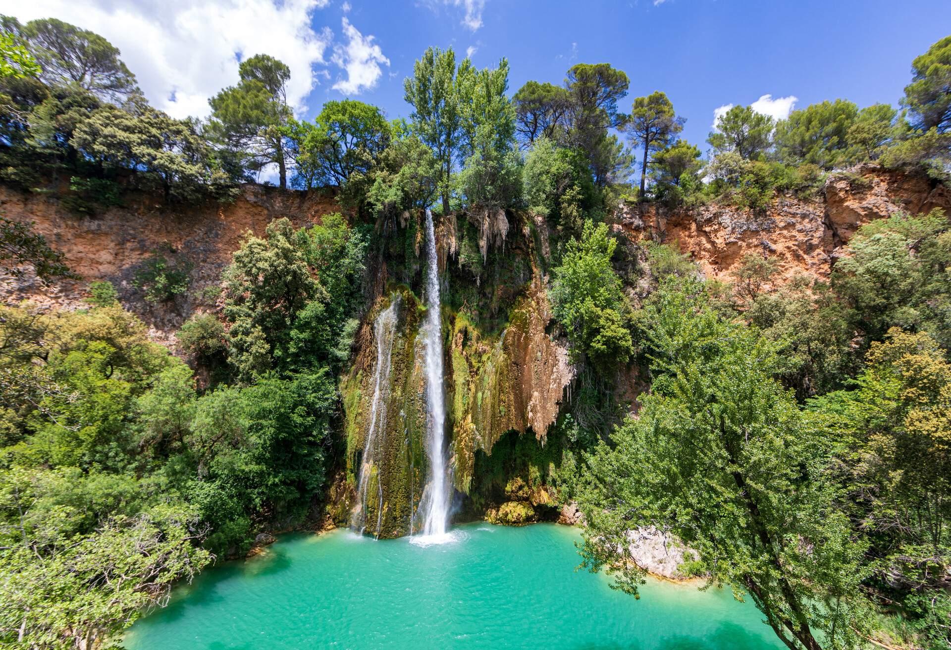 A low-volume waterfall in a jungle flows into a tranquil stream.