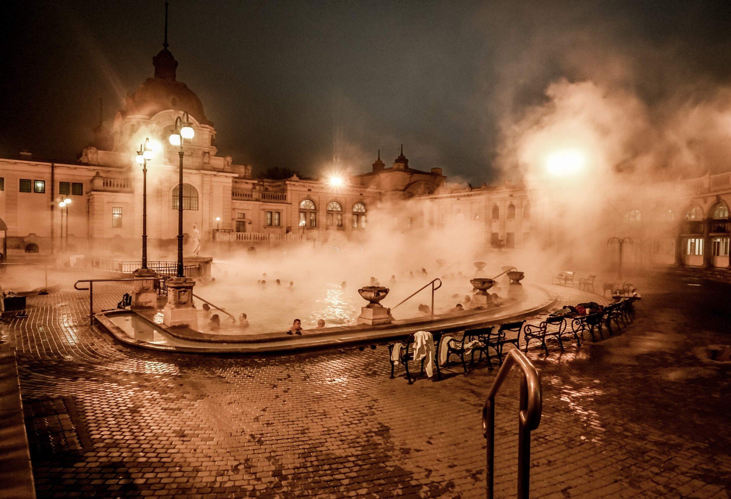 People dip in a thermal pool with a cloud of steam.