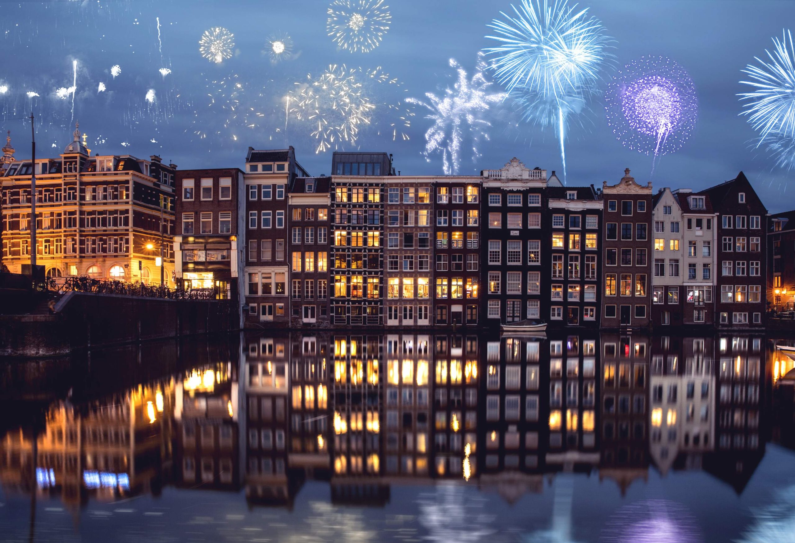 Fireworks bursting in the night sky above the canal-side buildings.