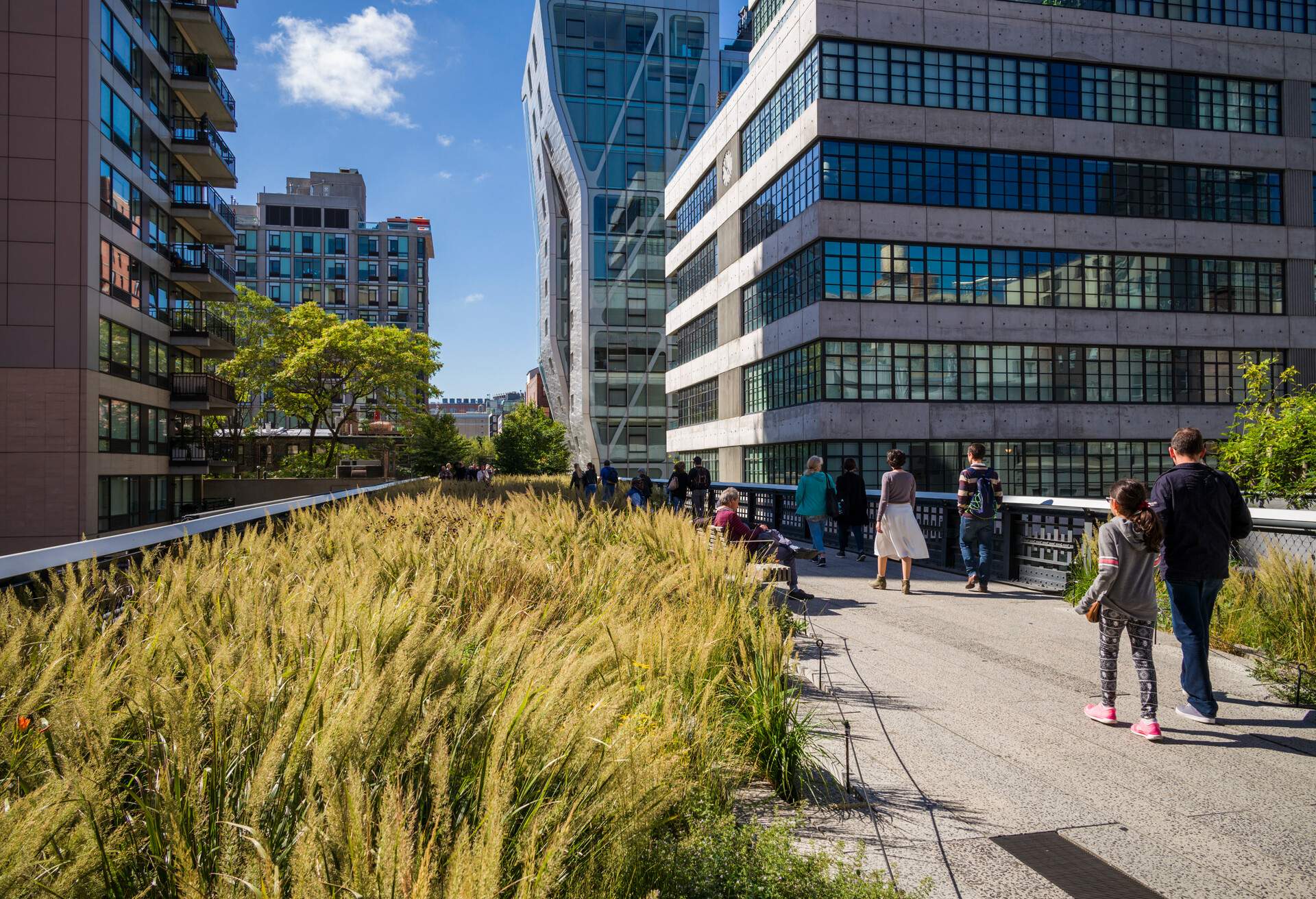 People strolling down a walkway alongside contemporary buildings with glass windows.