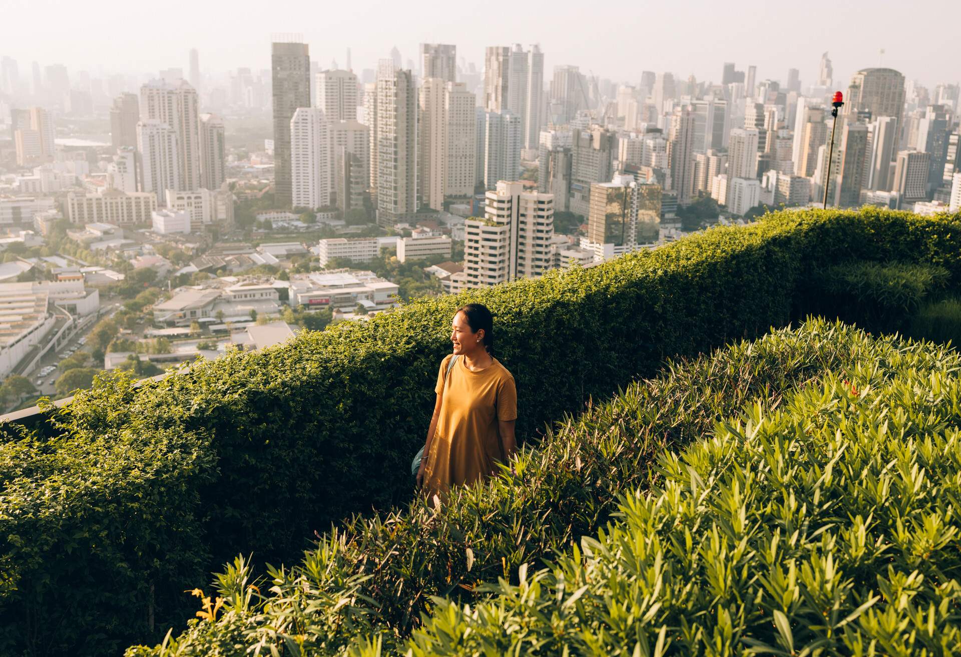 A happy Thai woman walking in the park with the cityscape behind her.