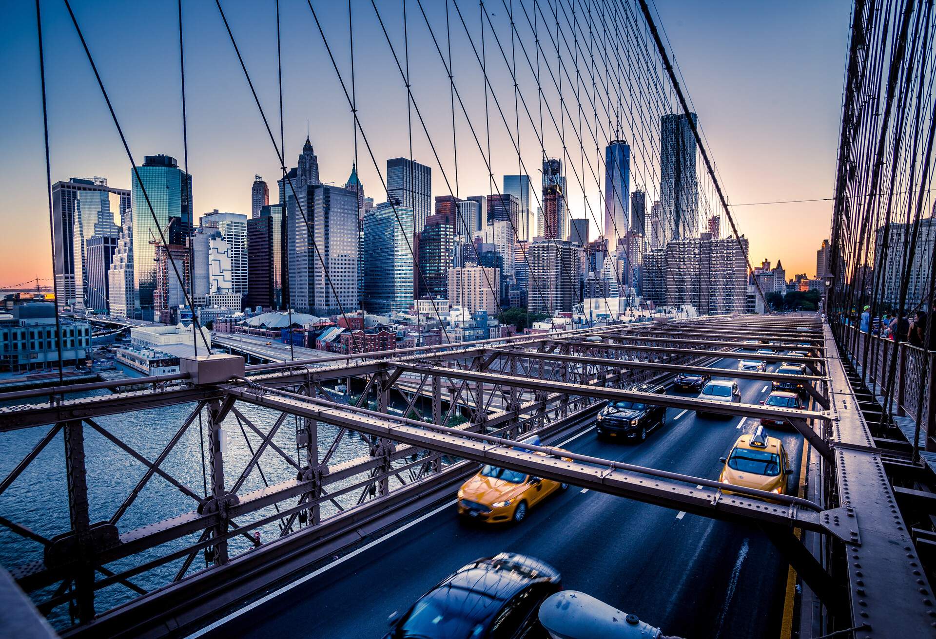 Cars speeding across the Brooklyn Bridge during a vibrant sunset, offering a captivating view of the iconic towering skyscrapers of Manhattan in New York City.