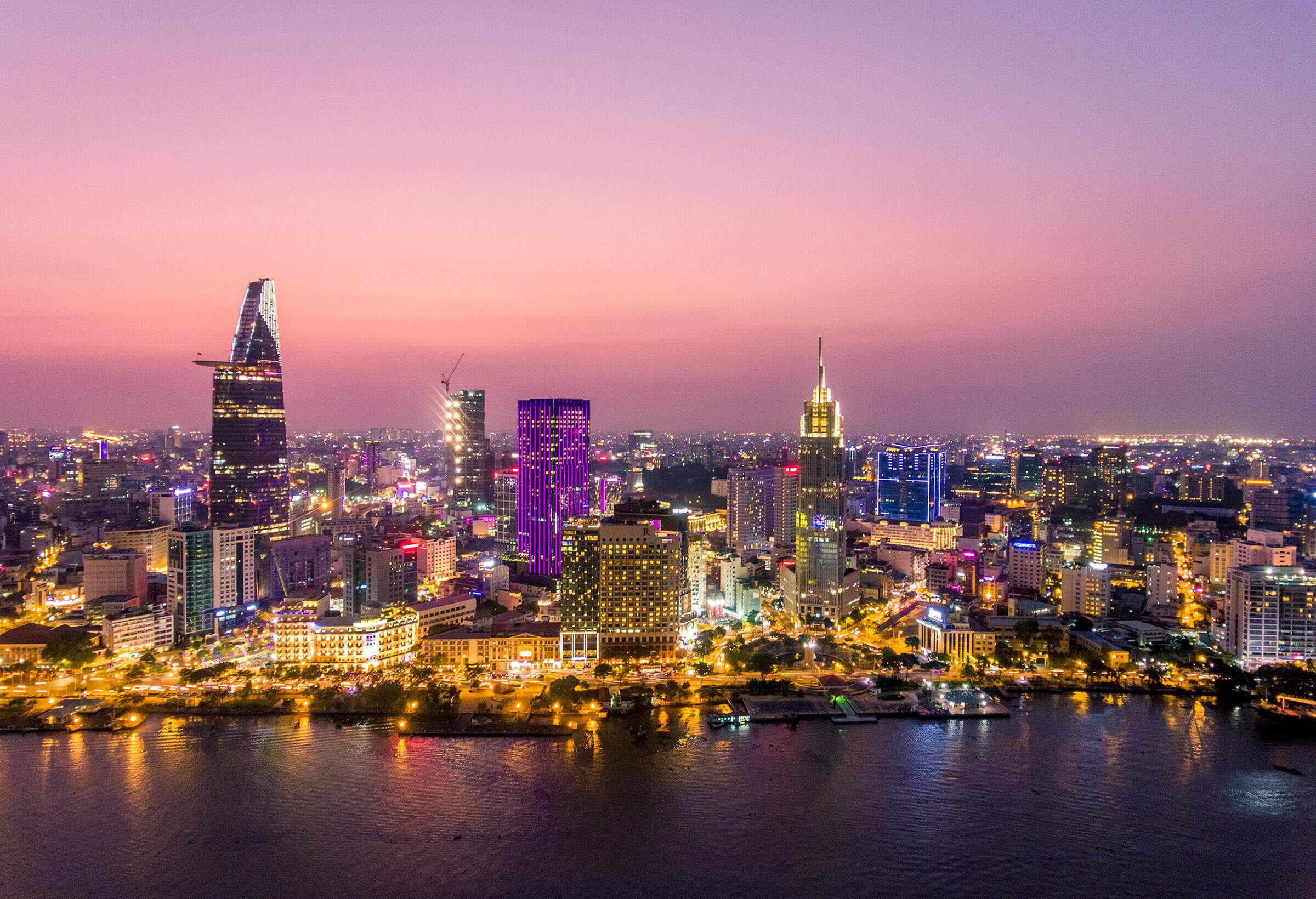 Compact buildings of a populous city sprawling on the vast valley, illuminated at night alongside the broad river.