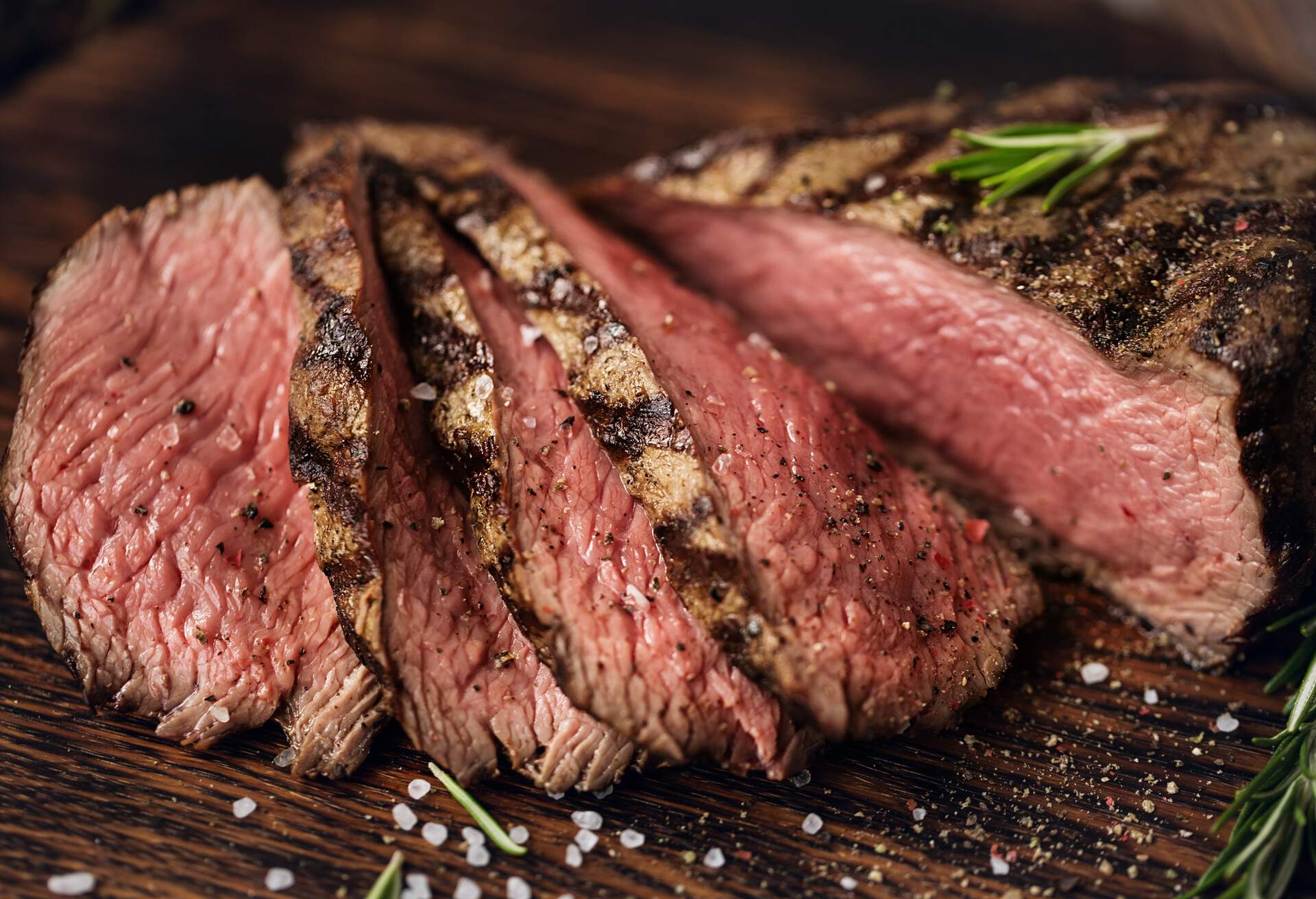 Juicy medium Beef Rib Eye steak slices on wooden board with herbs spices and salt. Ready to eat steak with ingredients on a cutting board.