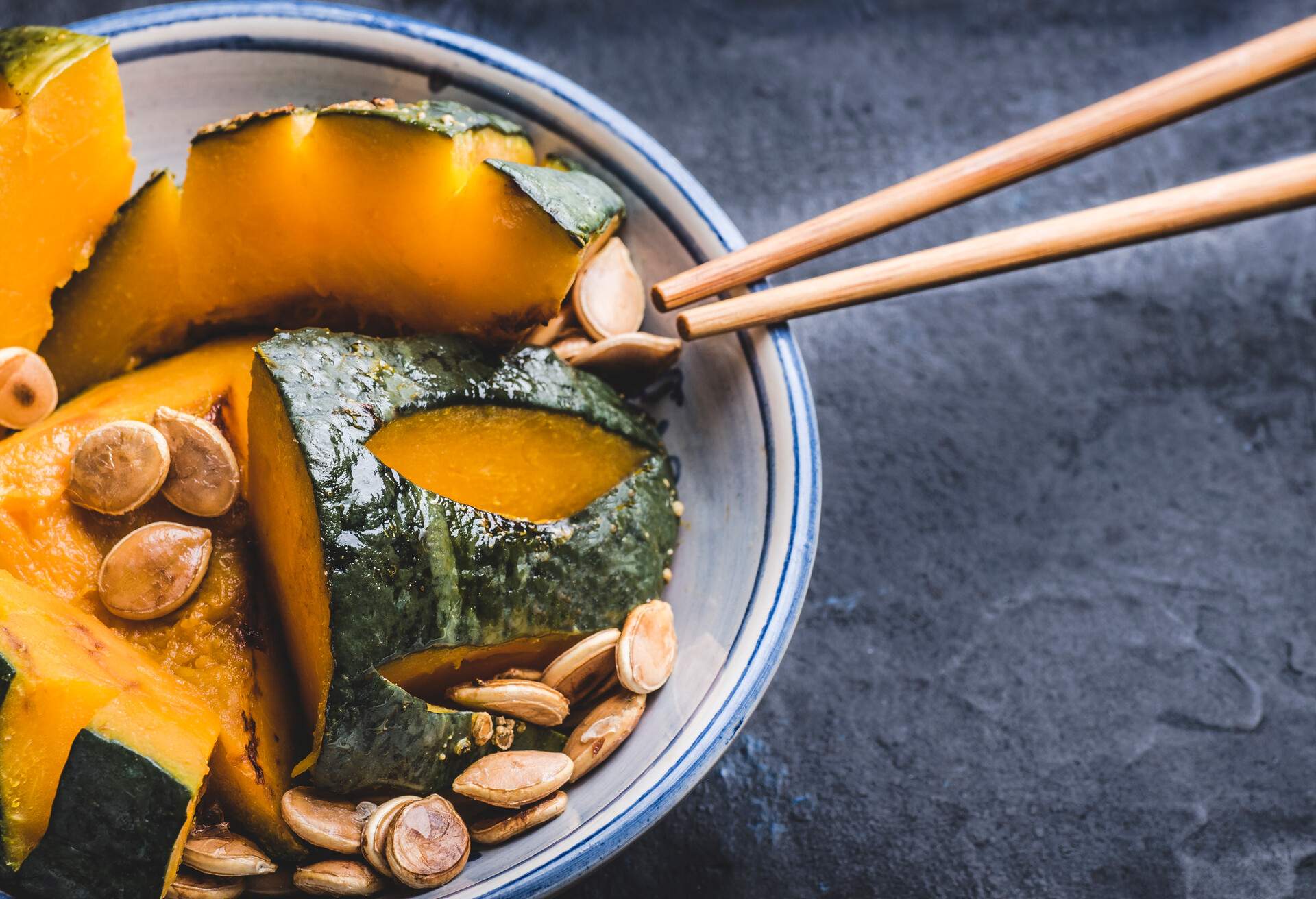 Delicious  Kabocha Squash (Japanese Pumpkin) recipe. Japanese Simmered Kabocha cooked in savory dashi broth seasoned with soy sauce and sake with pumpkin seeds, close up, dark background. Web banner