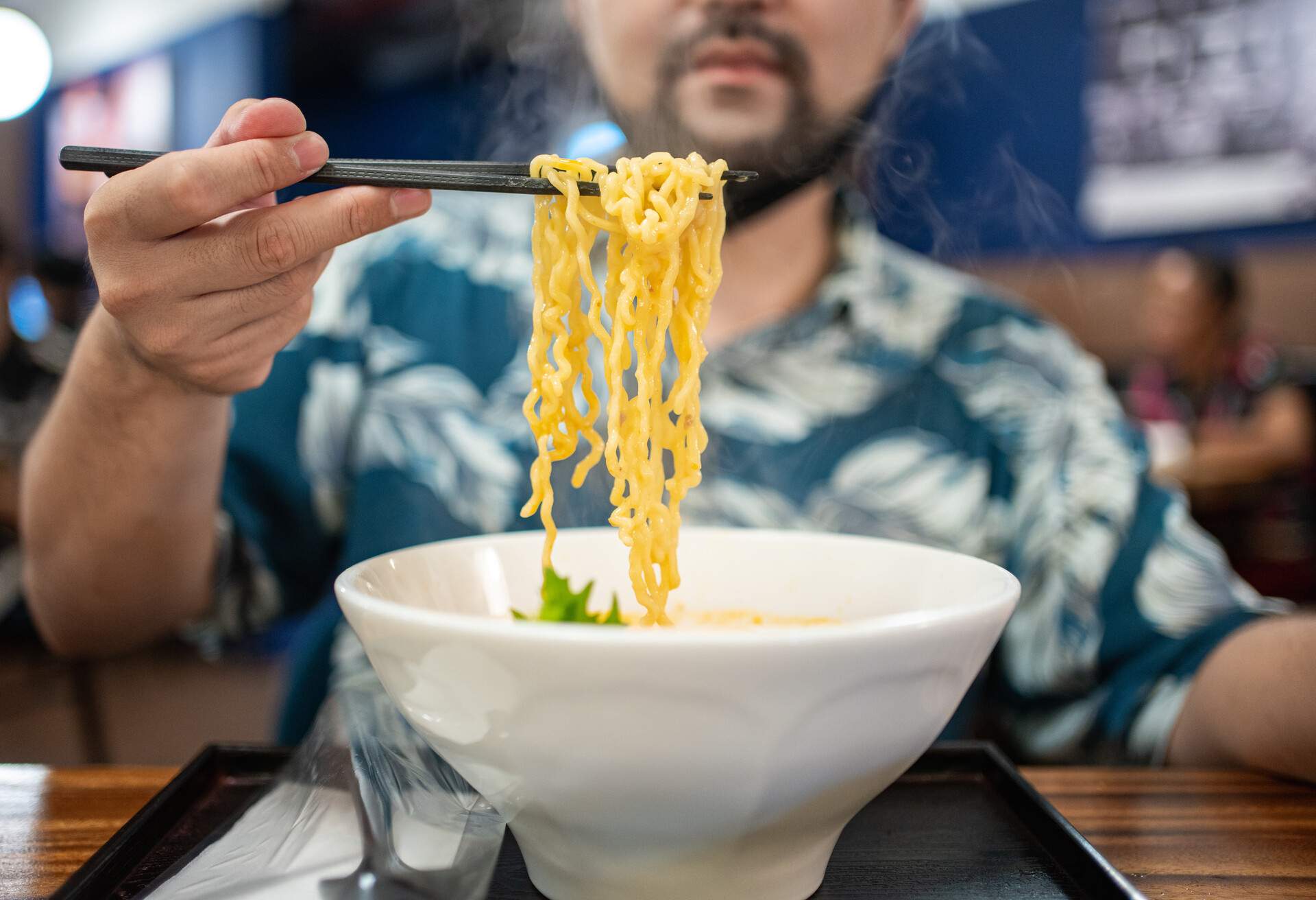 Close-up of man eating ramen soup with noodles, pork and egg