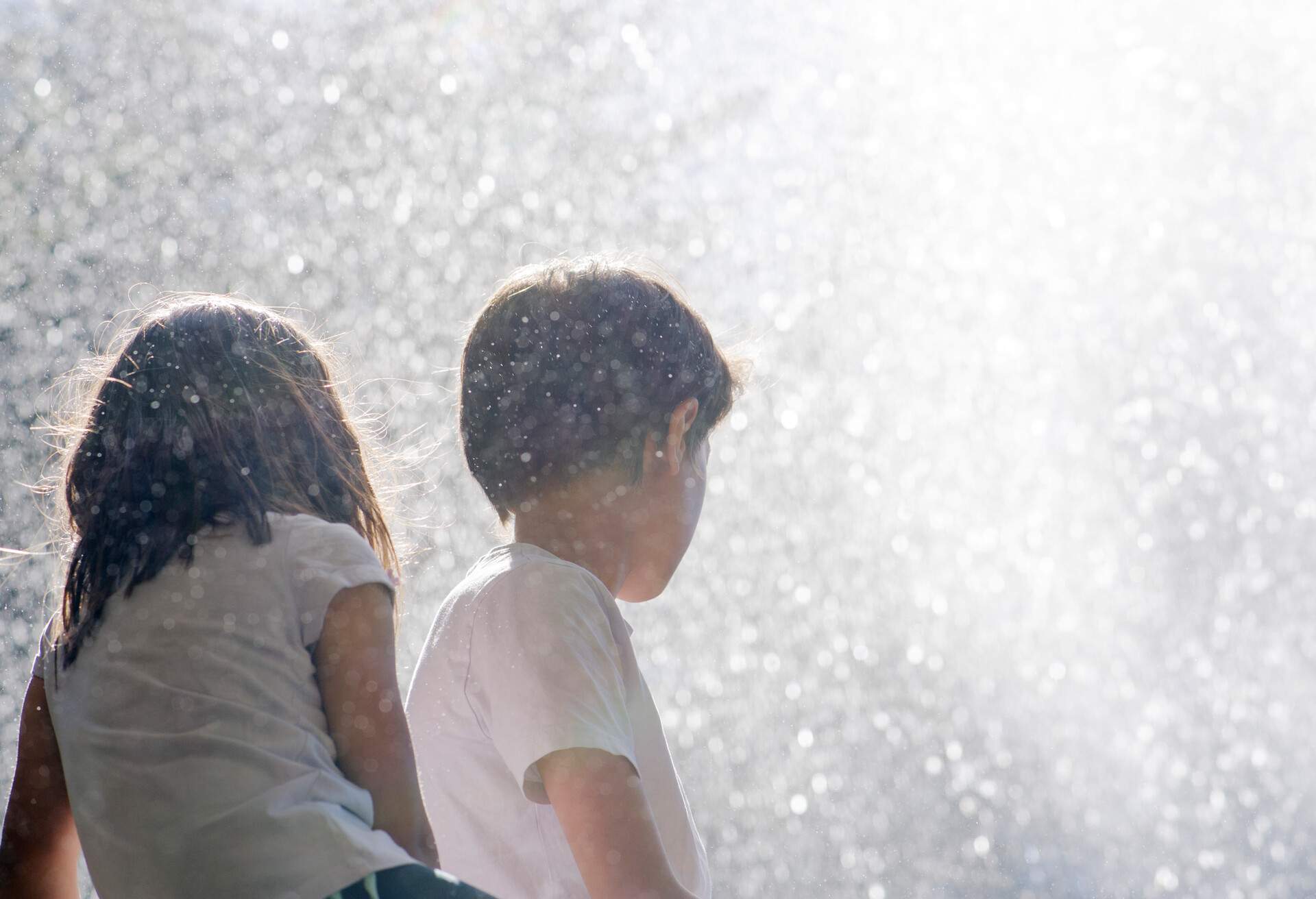 Two children in white shirts enjoying the spray of water. 