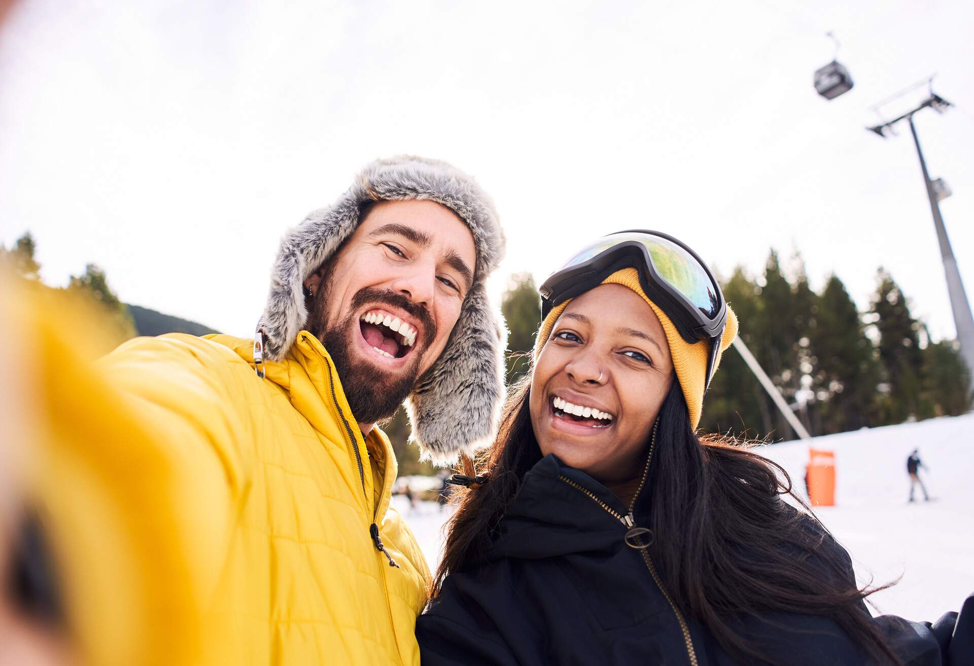 Selfie of a happy young couple in the ski slopes, smiling at camara wearing yellow