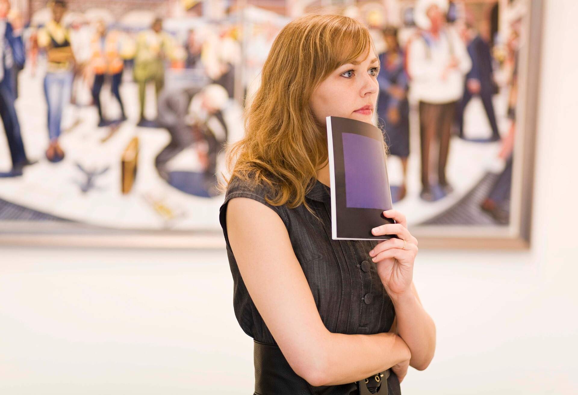 A young blonde lady holds her notebook on her chin in deep thought inside the museum.