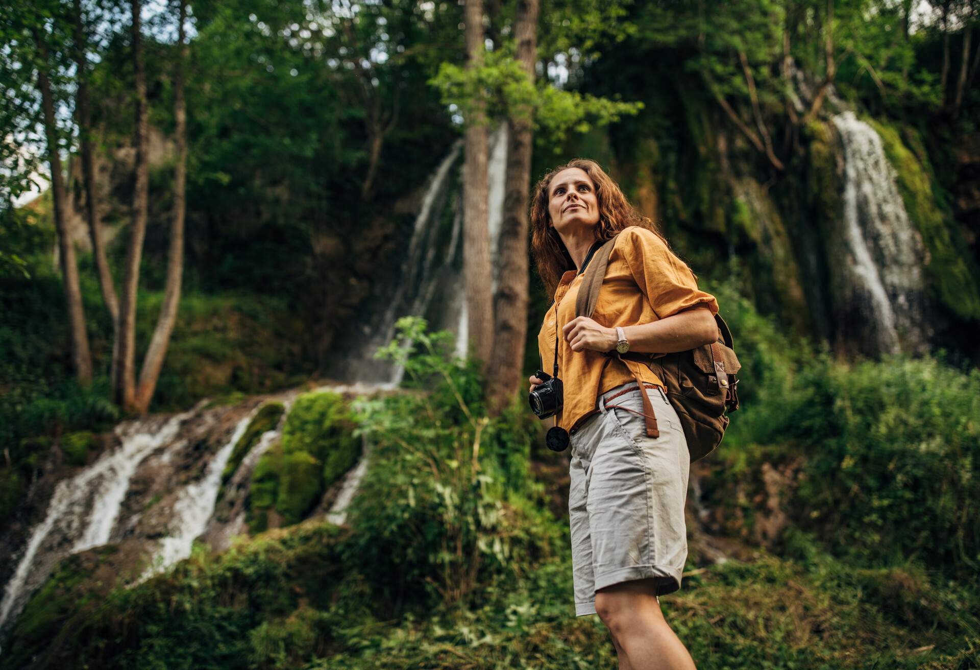 One woman, lady explorer and biologist standing in nature by waterfall alone.