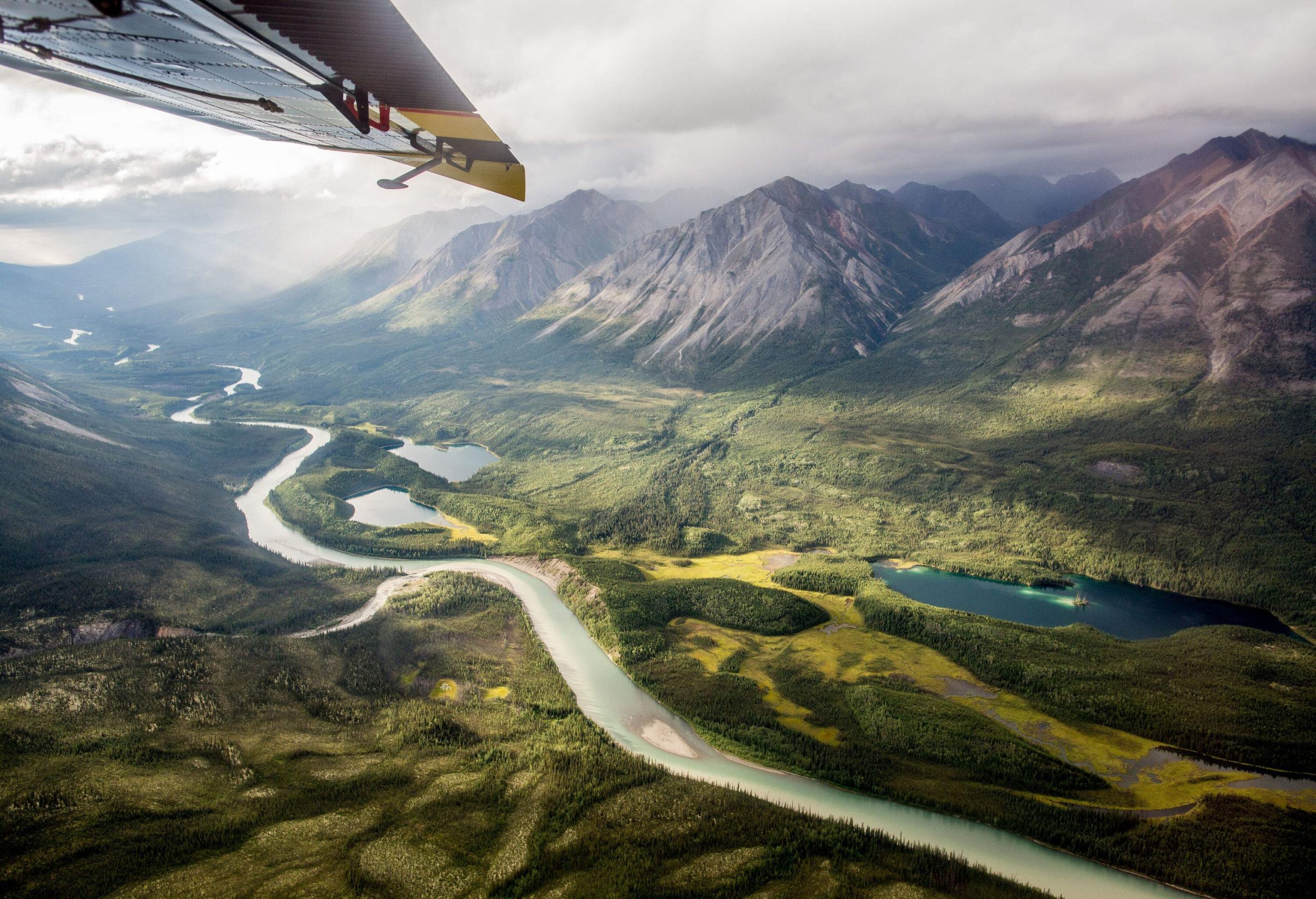 A meandering river courses through pristine wilderness, framed by abundant trees in a national park, with a majestic mountain range looming in the near distance.