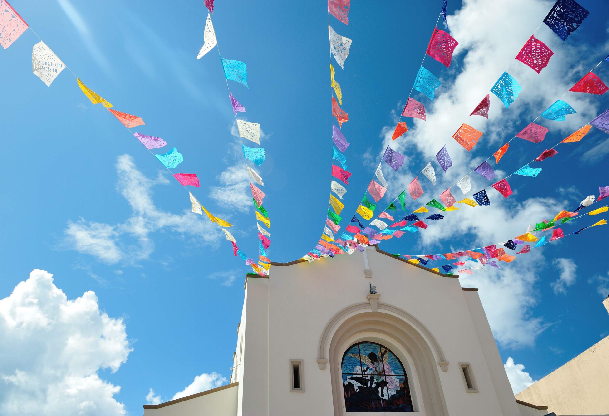 Colourful small flags hang in front of a white facade church.