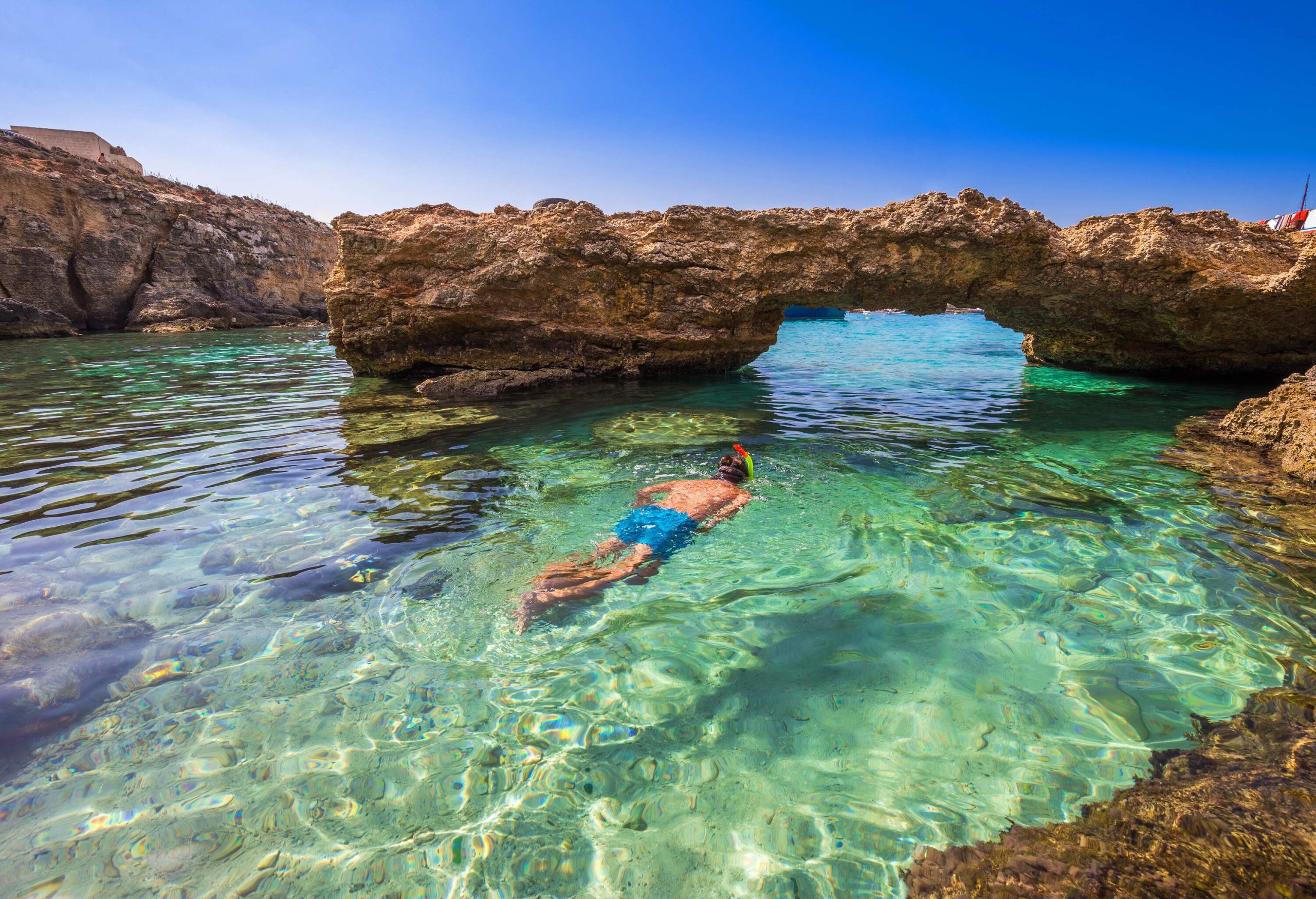 A person snorkelling on the clear waters of a lagoon with unique rock formations.