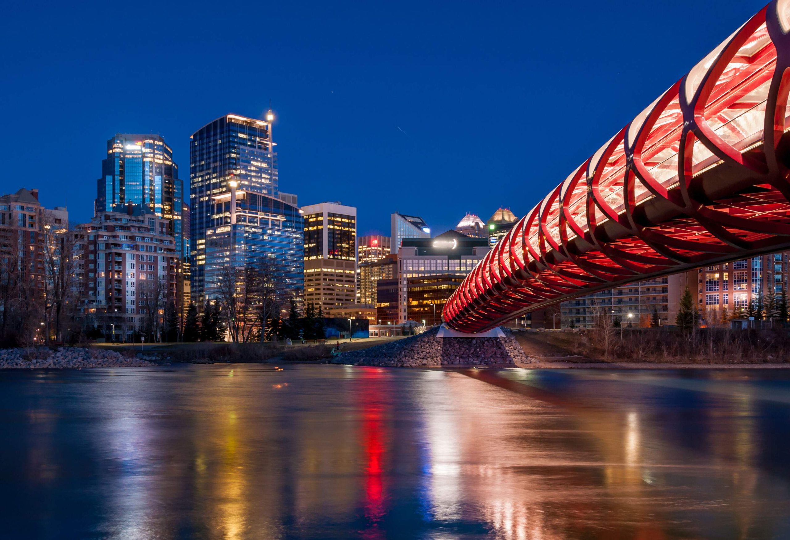 A modern pedestrian bridge spanning over the river overlooking the brightly lit skyline with towering buildings captured at night.