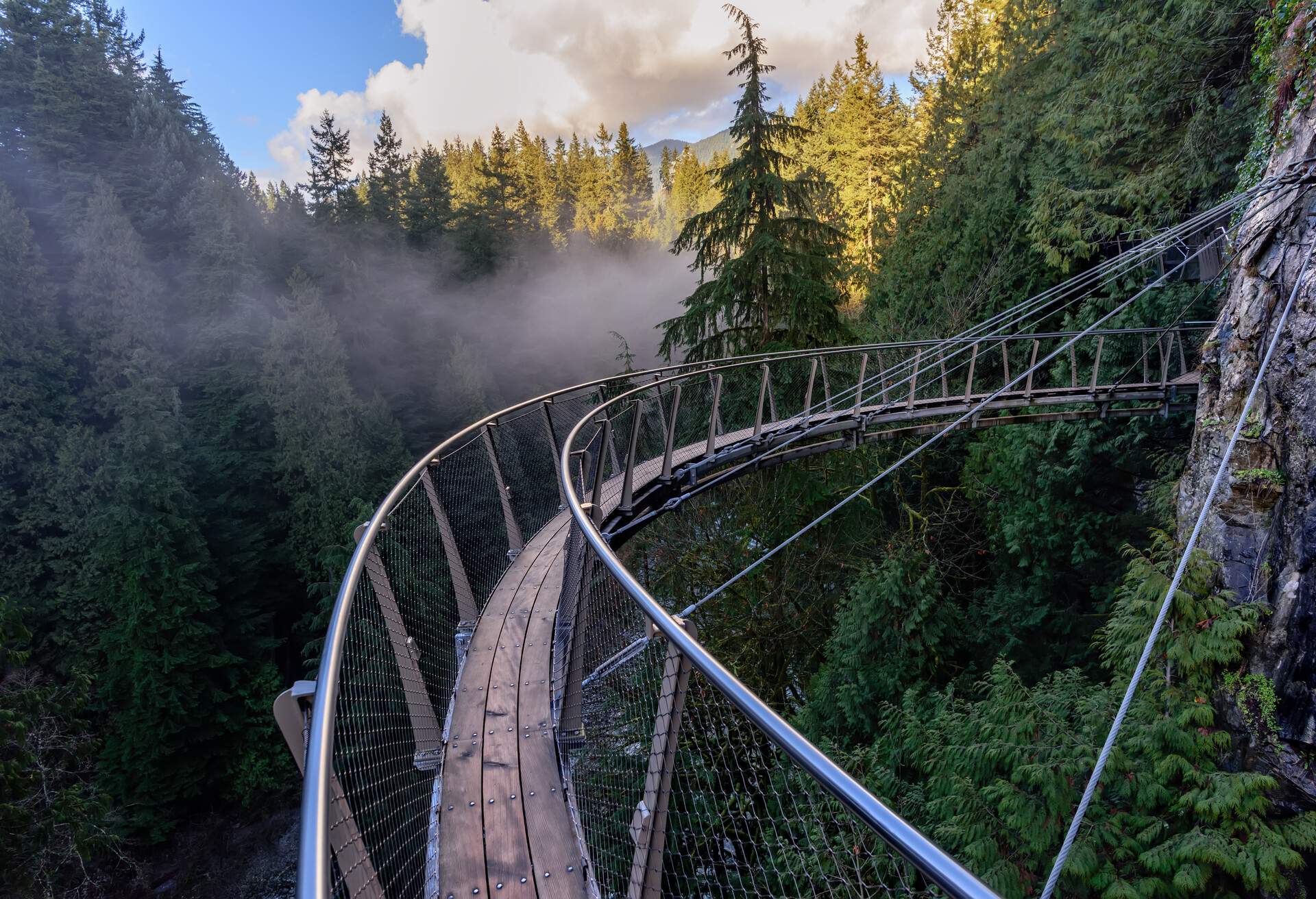 a view from above from the suspension bridge on rough streams of a mountain river among green forests white fog and rocky mountains in a sunny, summer day