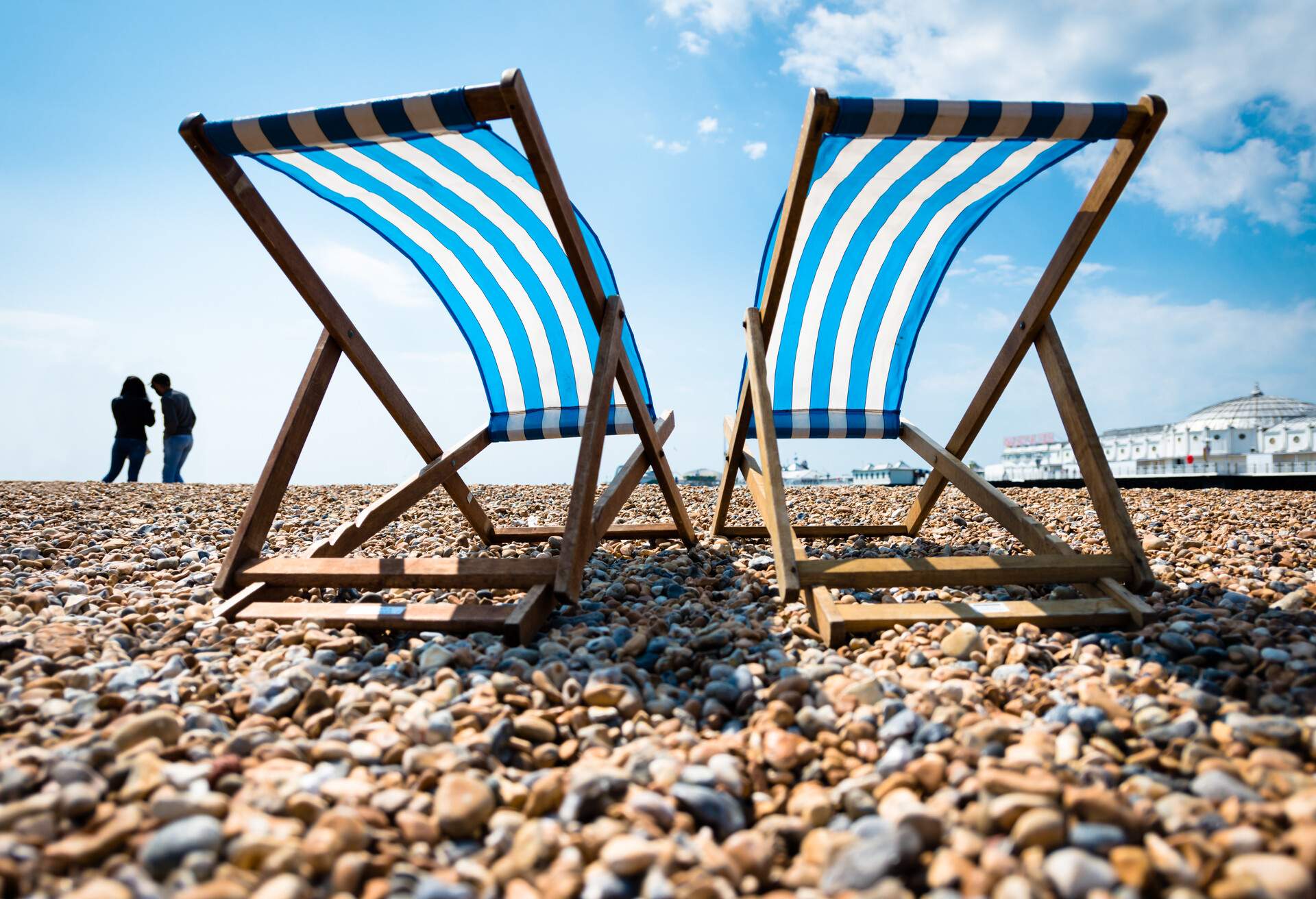 Silhouette of young couple and two empty deck chairs on the beach at Brighton with the Palace Pier in the distance.
