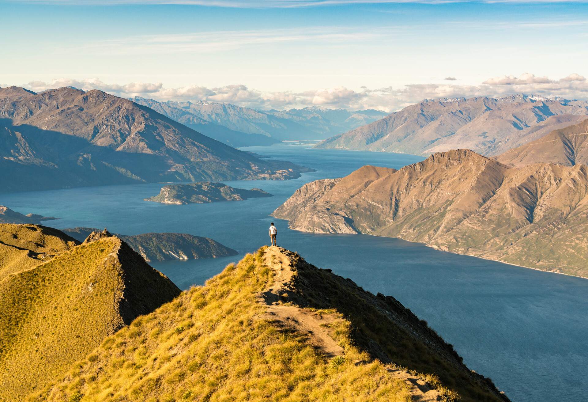 A man on top of a mountain with a view of a river and mountain ranges.