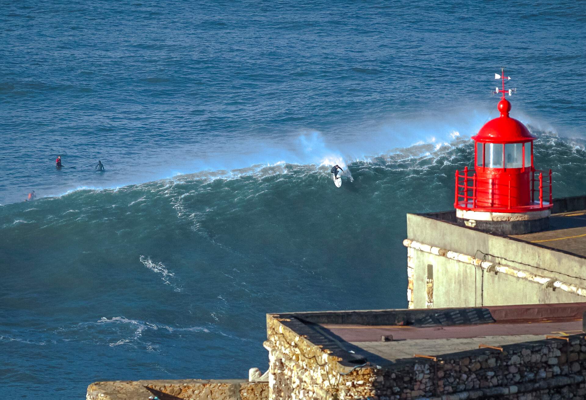 Surfers practice the sport near the lighthouse of Nazaré, Portugal, with one of the biggest waves in the world and also one of the most dangerous.