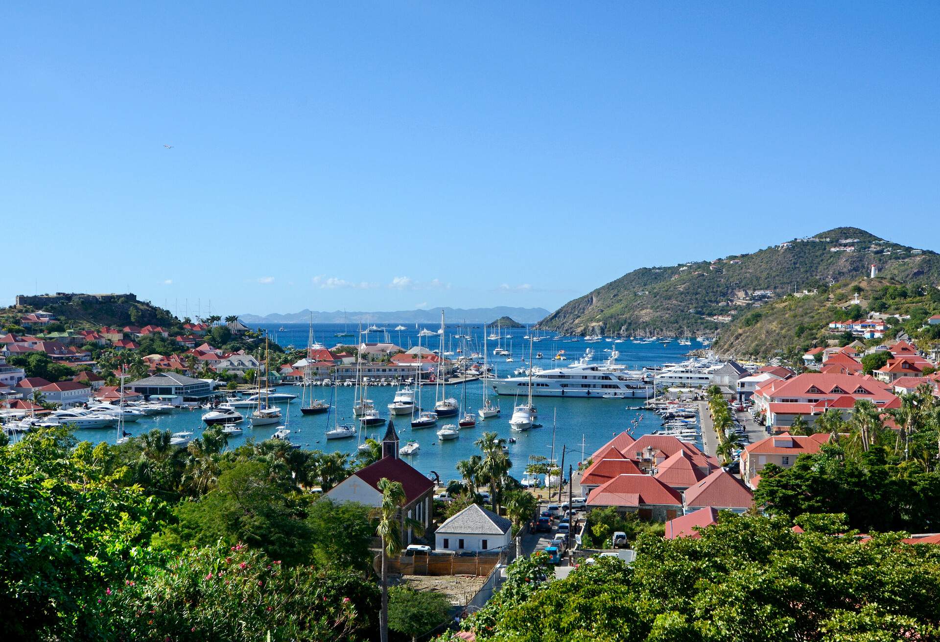 A coastal town with boats crowding the harbour, flanked by buildings and hills around the shore.